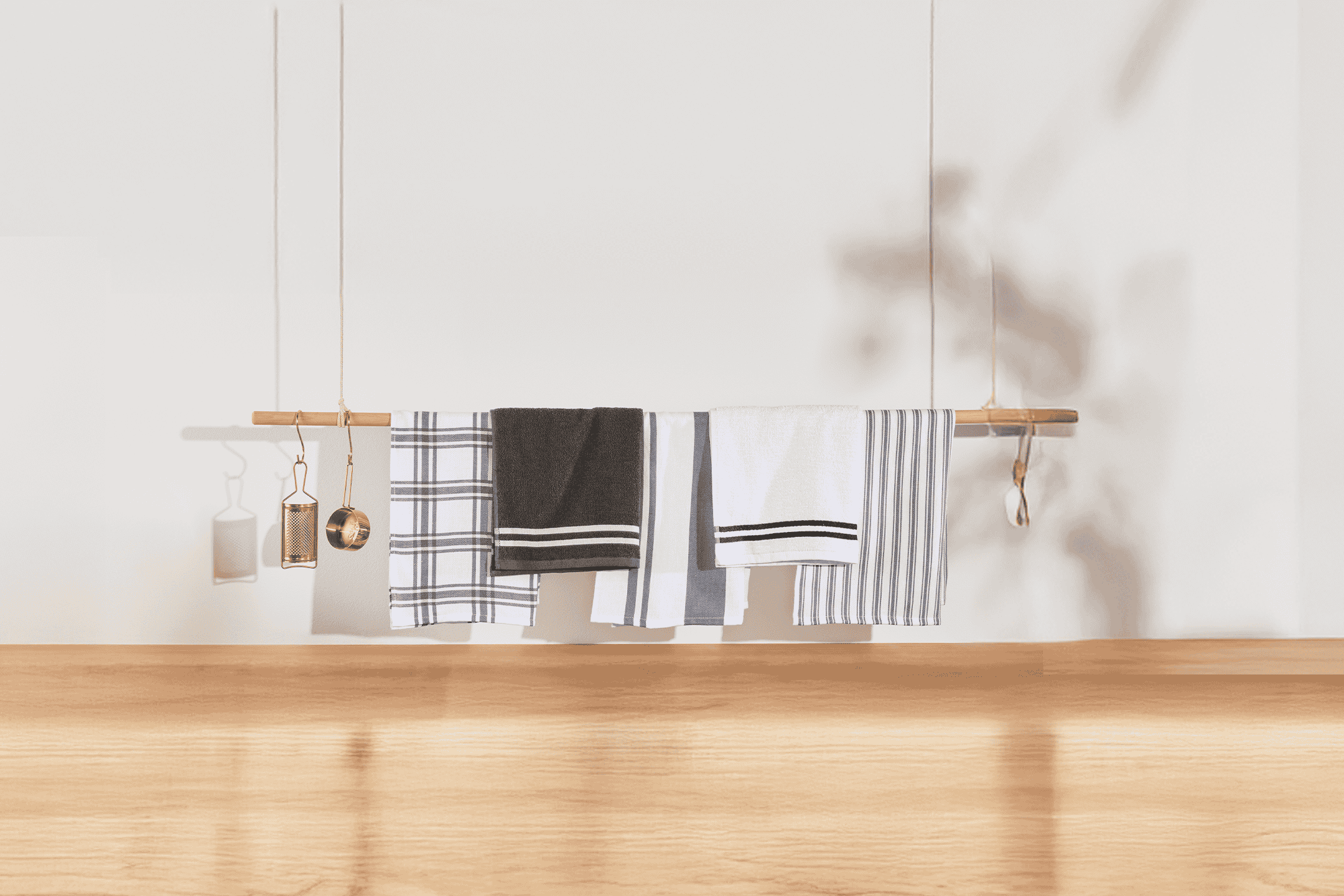 Køkkenhåndklæder i forskellige mønstre hængende på en træstang over et træbord.