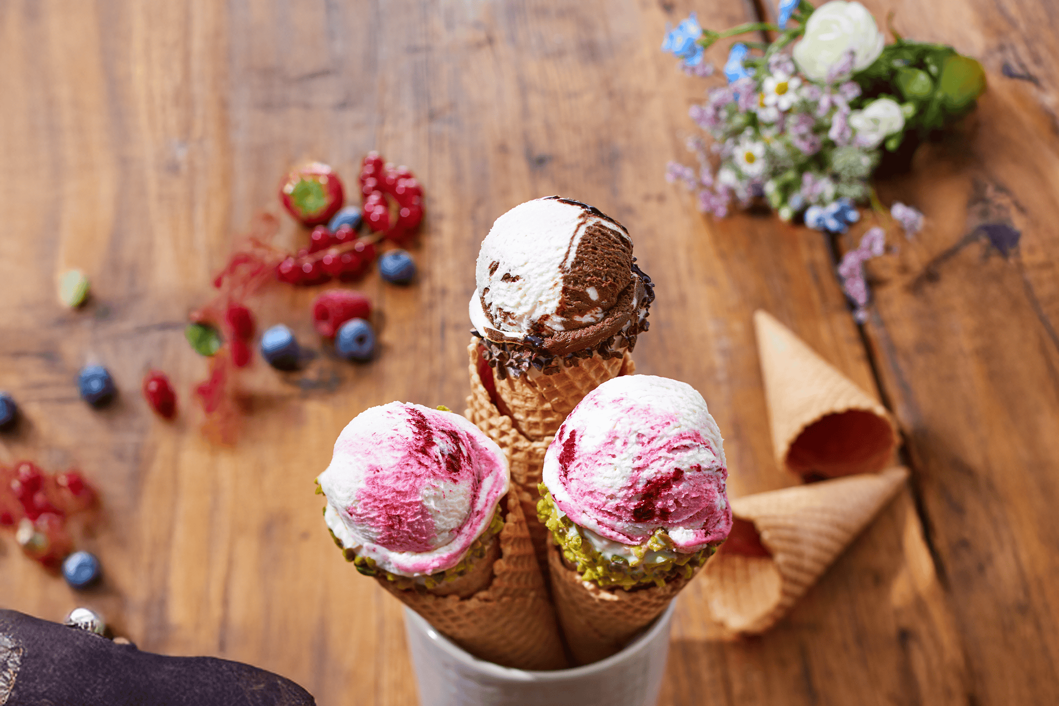 Tre isvafler med forskellige smagsvarianter og bær på et træbord.