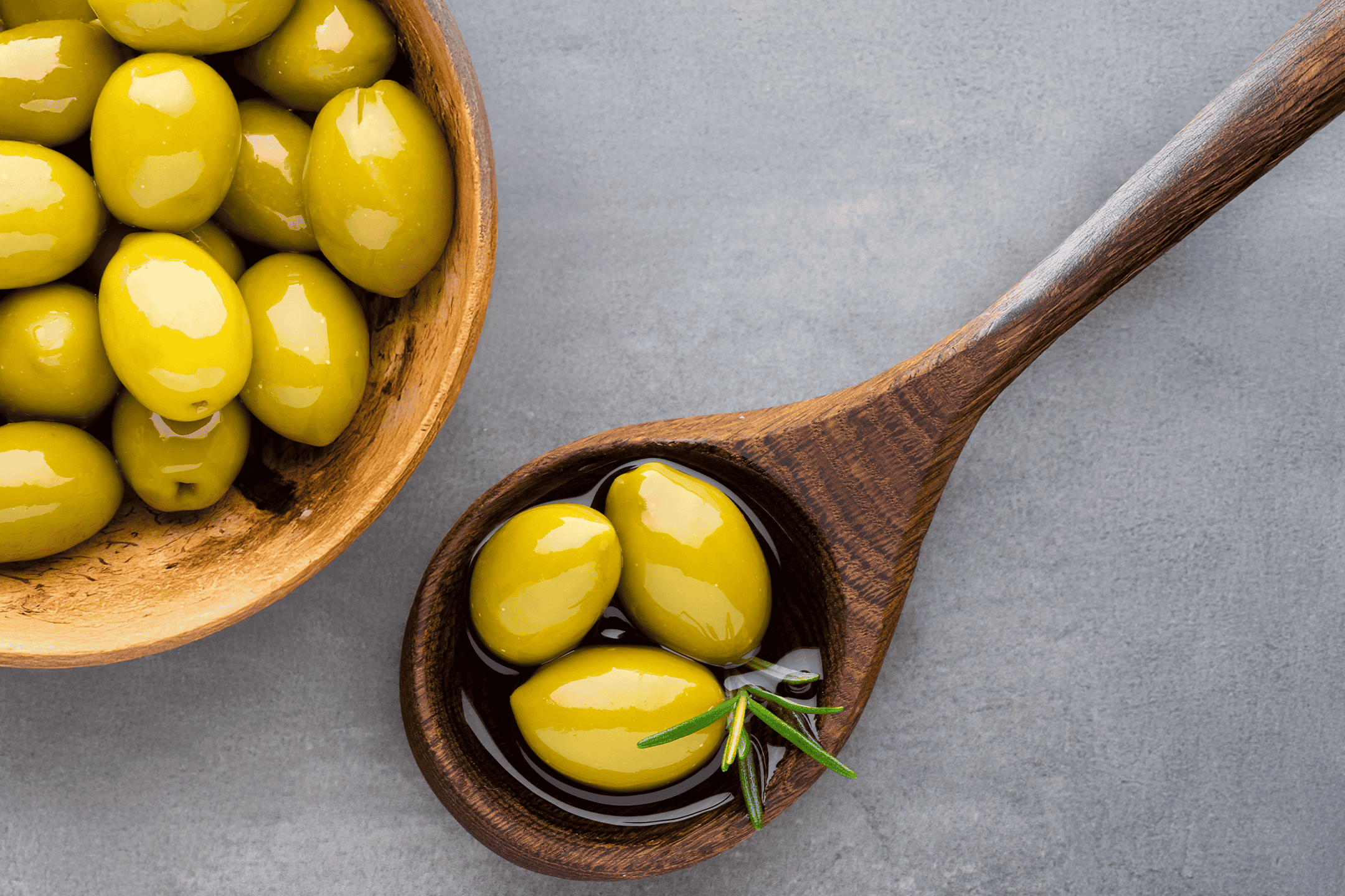 Grønne oliven i en træskål og på en træske med rosmarin.