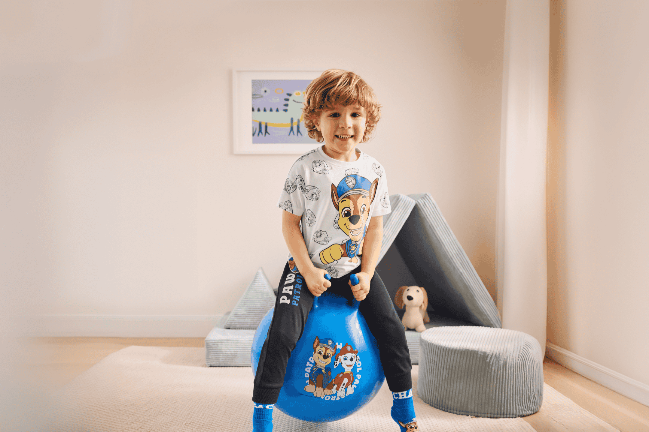 Glad dreng på en blå hoppebold med tegneseriefigurer, iført matchende tøj.