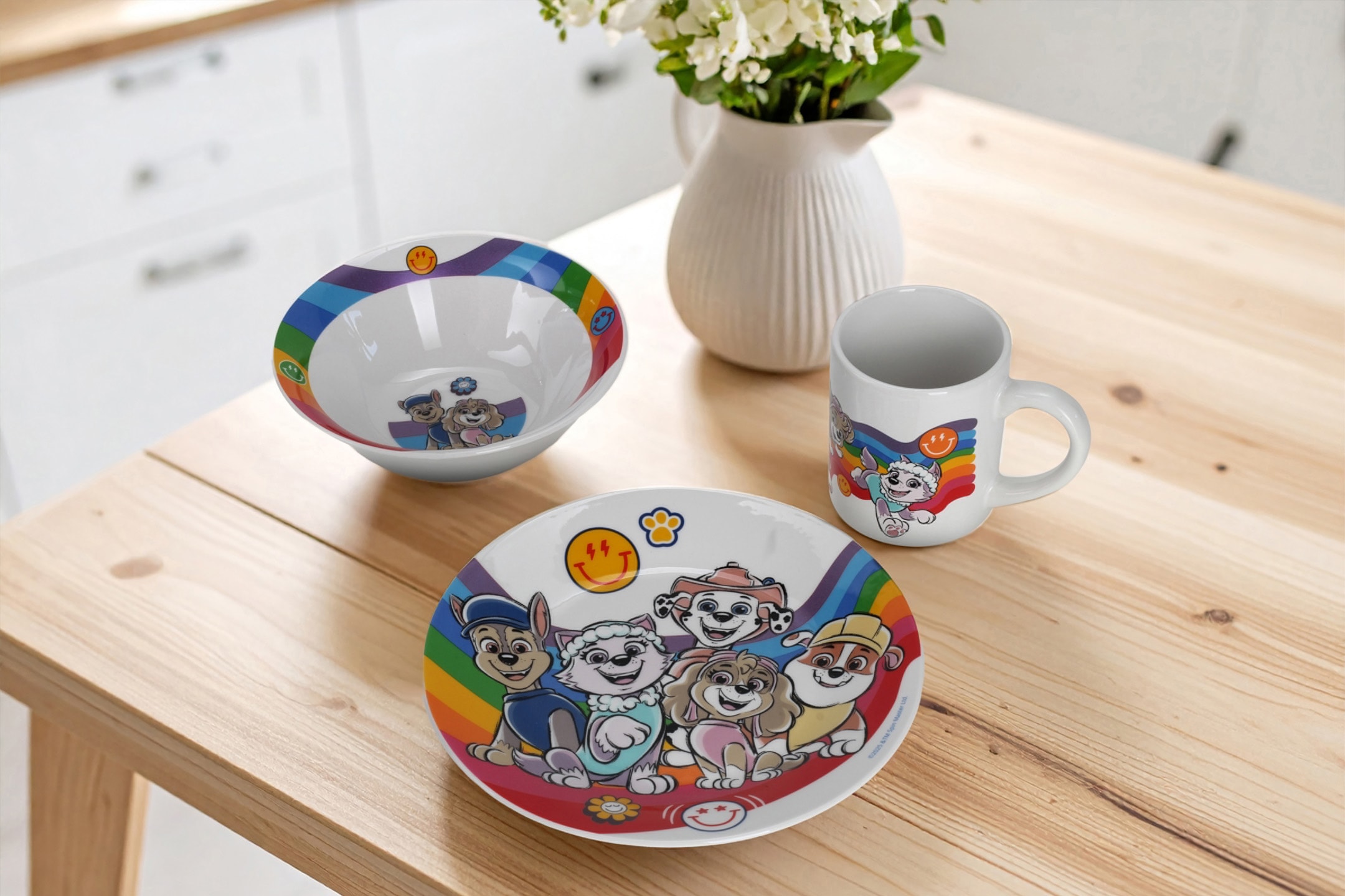 Børneservice med Paw Patrol-tema, inklusive en tallerken, skål og krus, på et træbord.