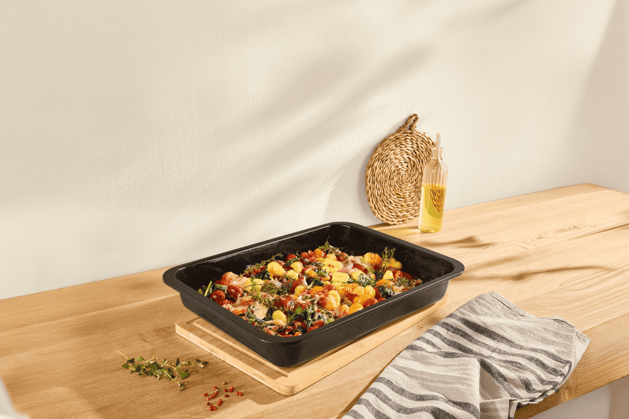 Bageplade med gnocchi, tomater og krydderurter på et træbord med en stribet klud.