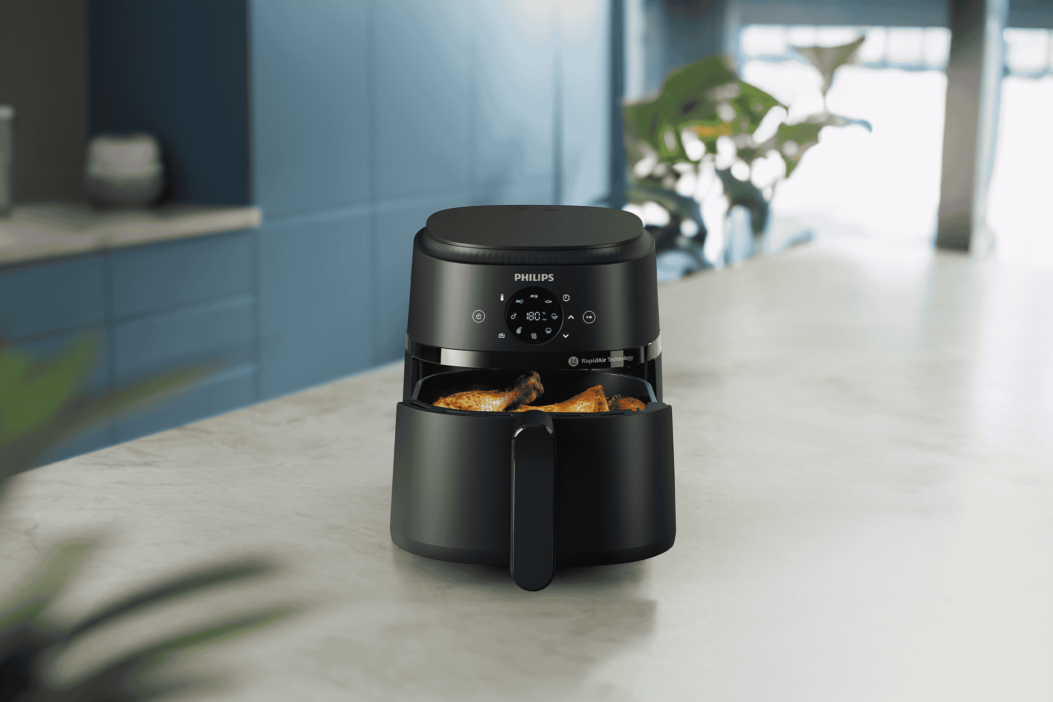 Sort airfryer med kyllingelår på en køkkenbordplade.