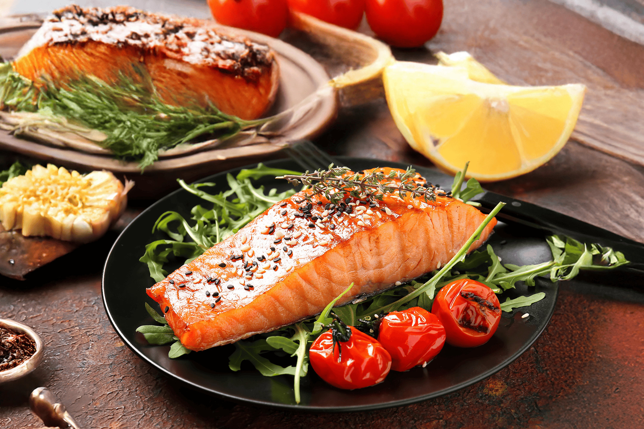 Laks med sesamfrø, cherrytomater og rucola på en sort tallerken.