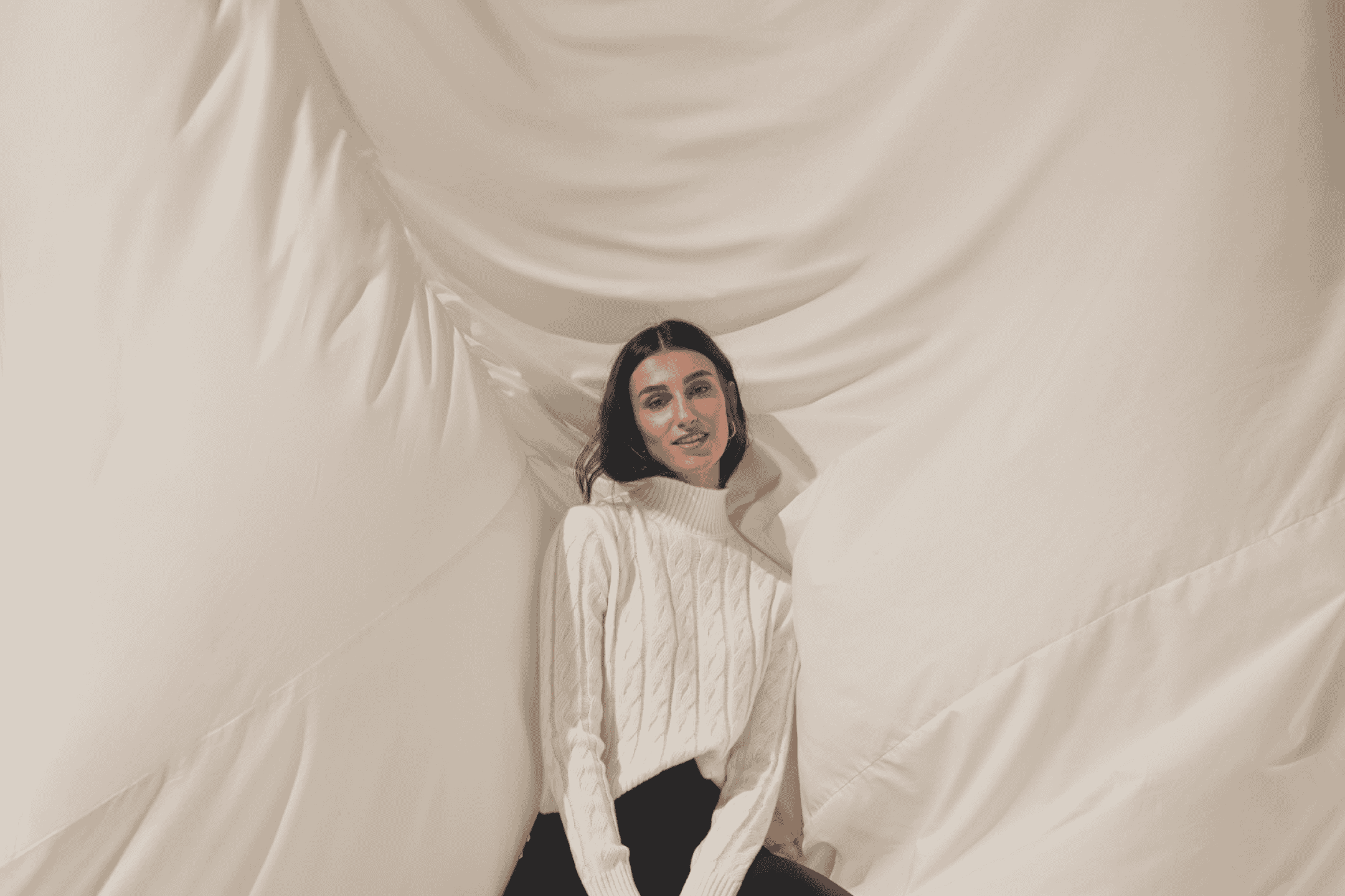 Kvinde i hvid striktrøje og sorte bukser, der sidder omgivet af hvidt stof.