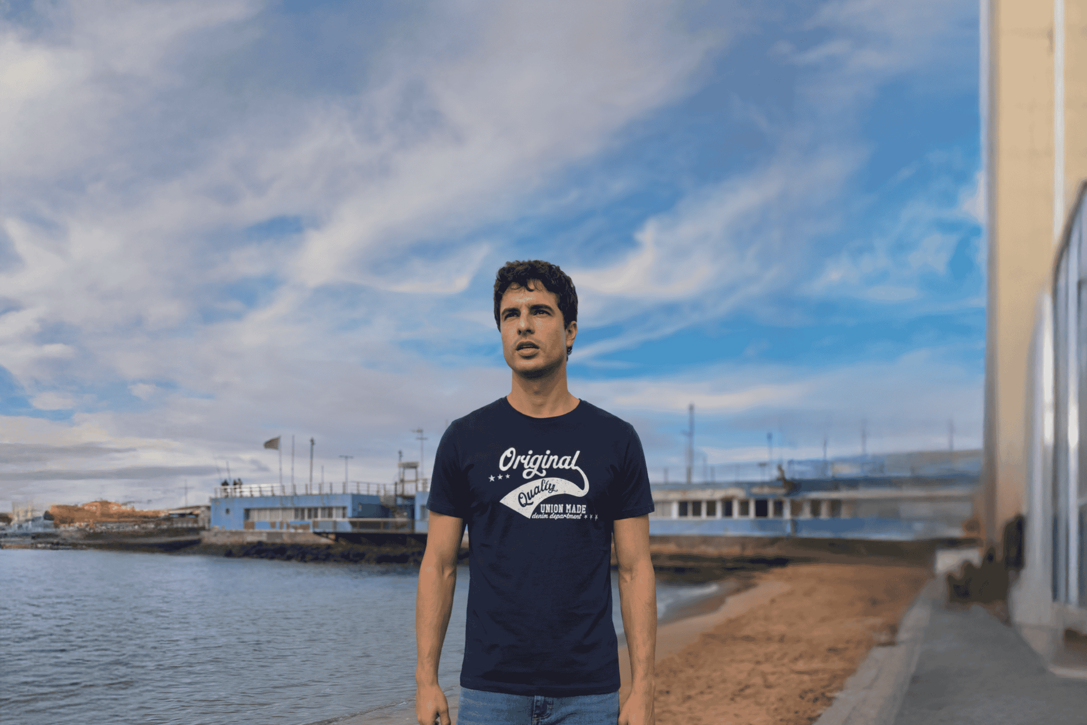 Mand i mørkeblå t-shirt med hvidt 'Original Quality' print ved vandet.