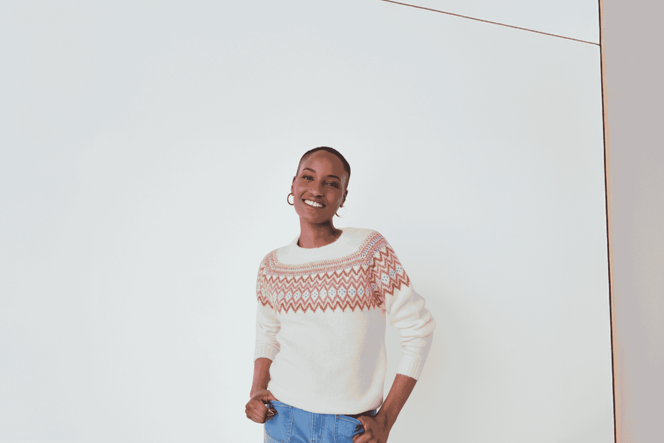 Kvinde i hvid striktrøje med mønster og jeans, smilende mod kameraet.