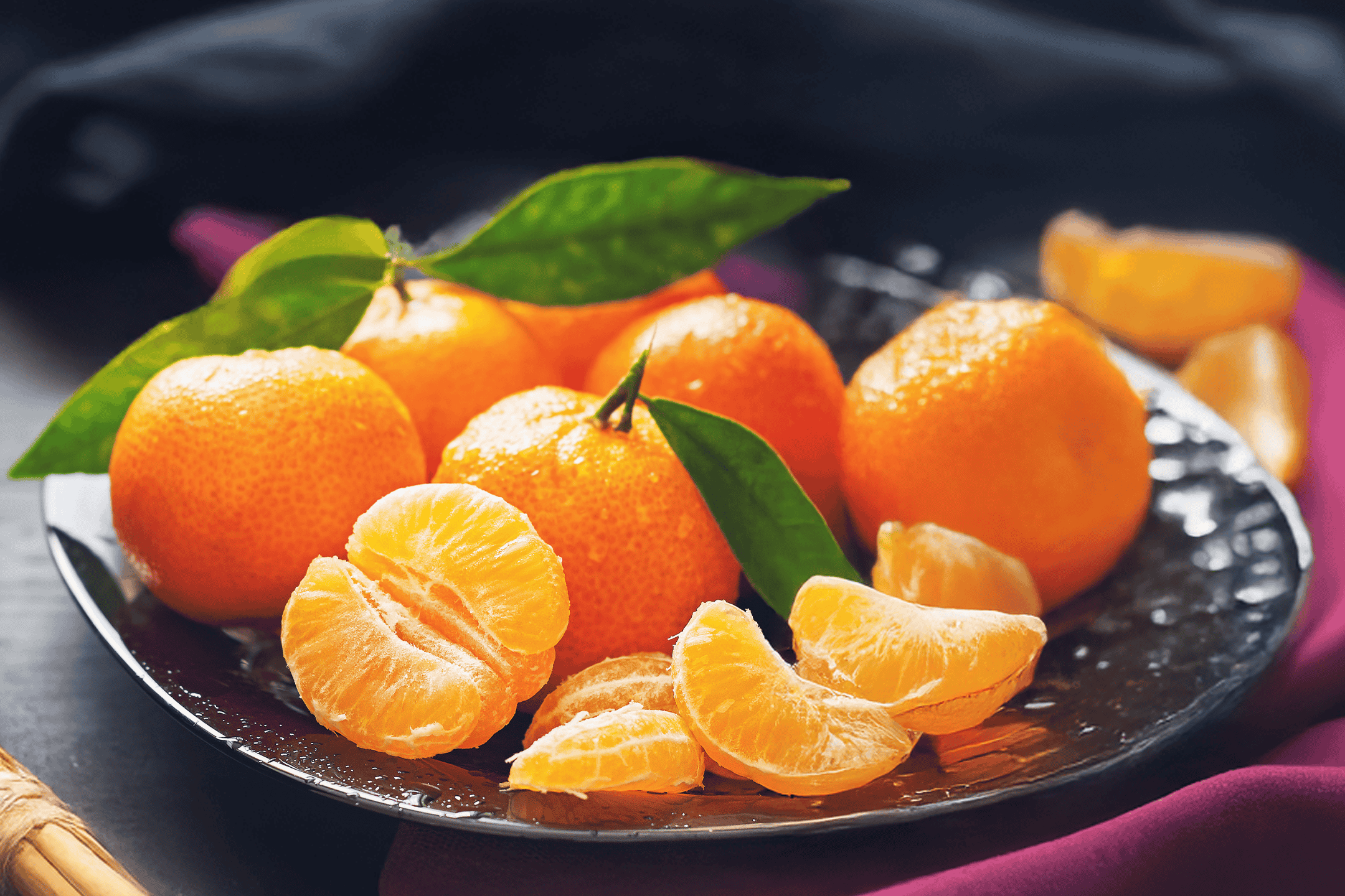 Friske mandariner med grønne blade på en mørk tallerken.