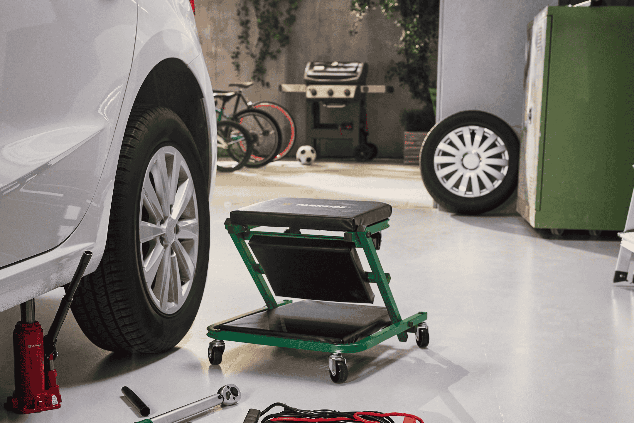 Bil på donkraft med mekanikerskamler og værktøj i en garage.