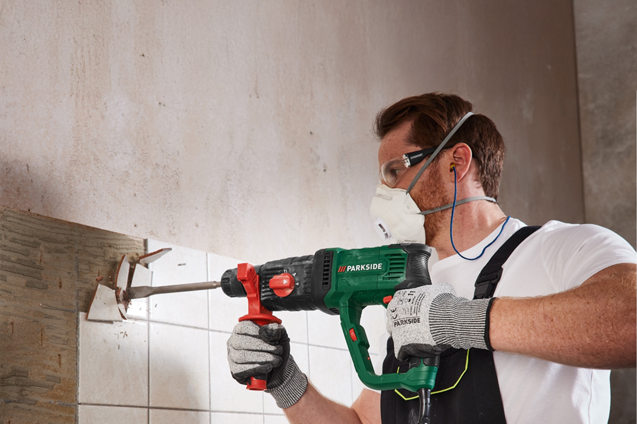 Mand med beskyttelsesudstyr bruger en borehammer til at fjerne fliser fra en væg.