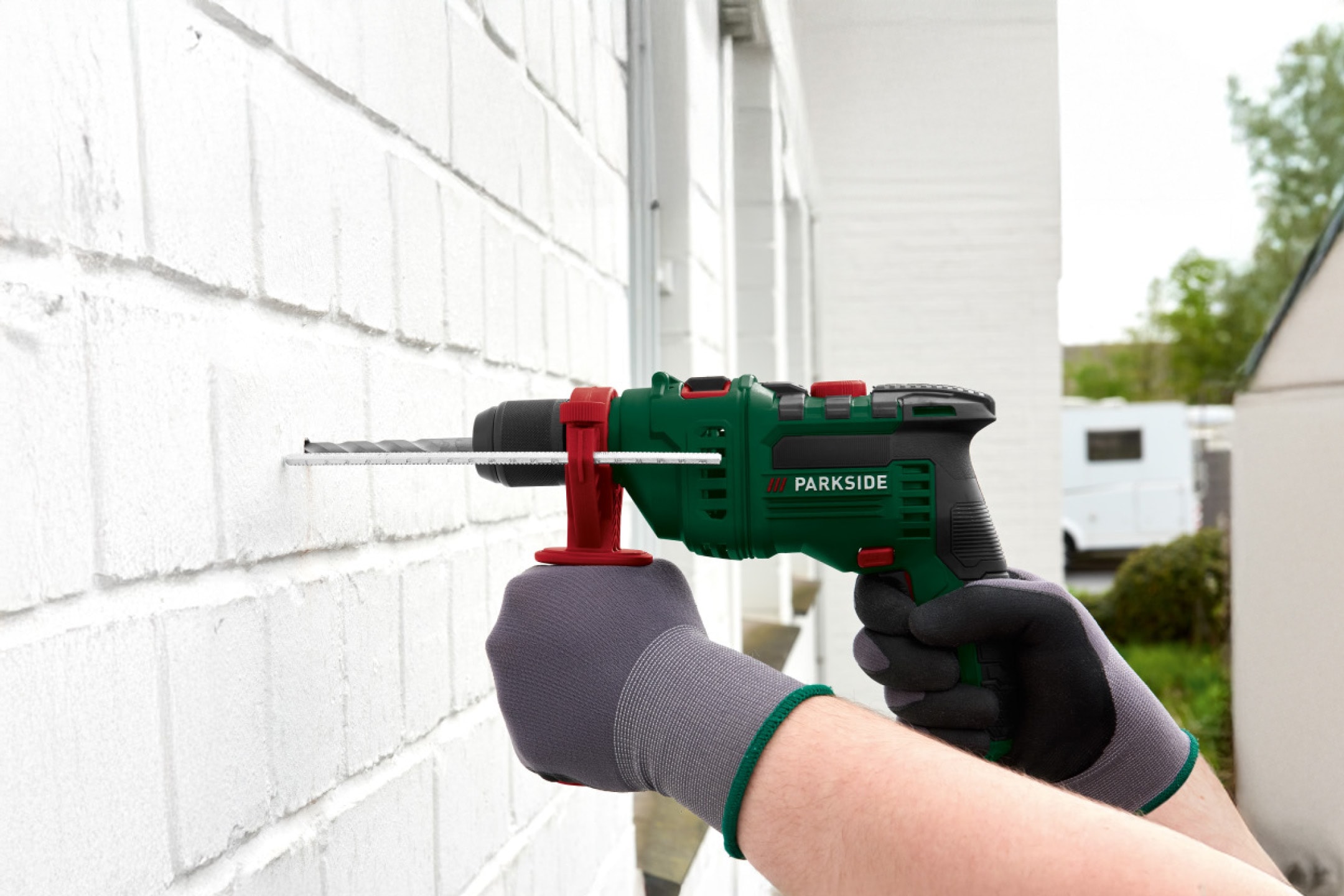 Person borer i en hvid murstensvæg med en grøn Parkside boremaskine.