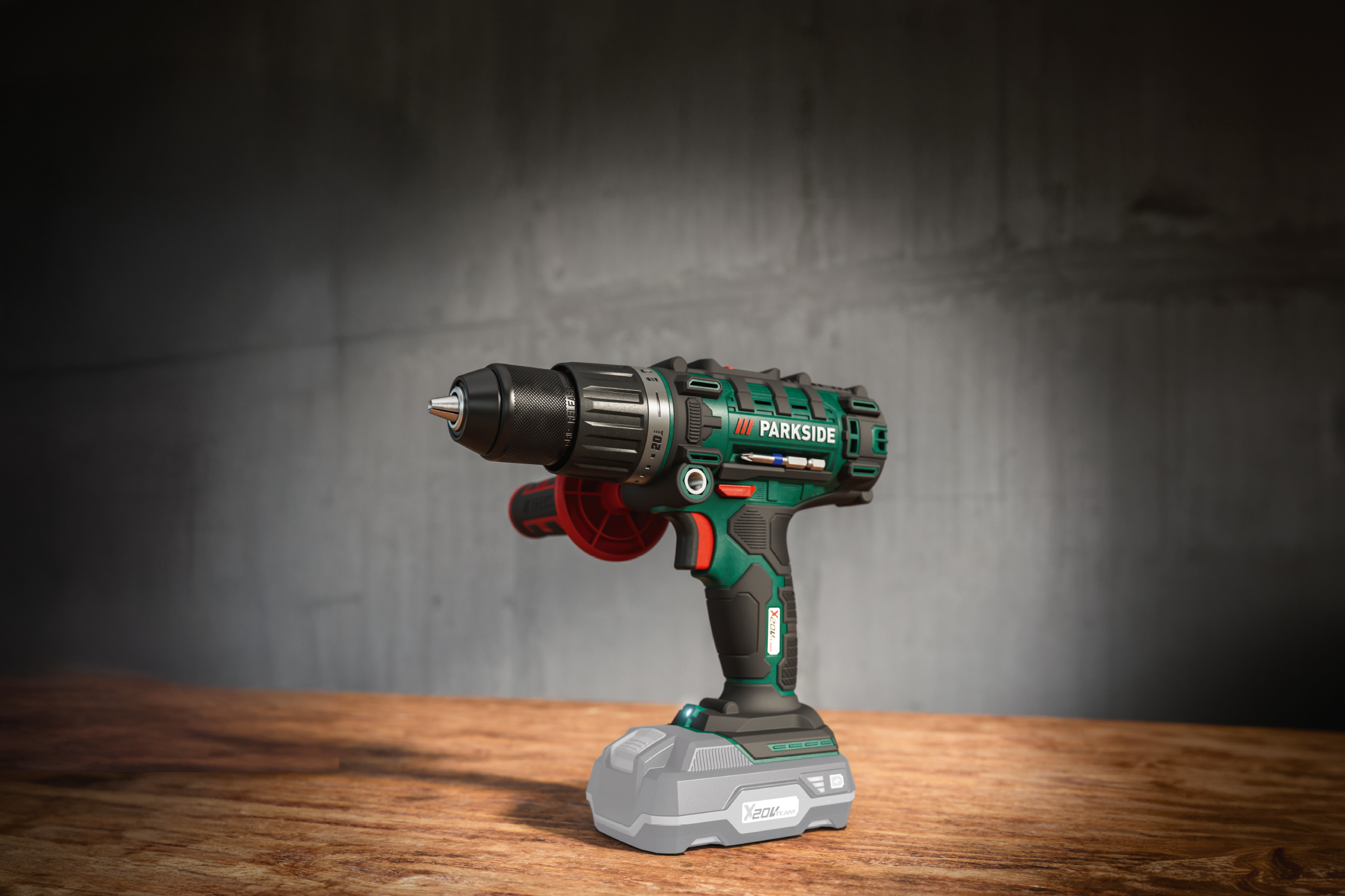 En grøn og sort boremaskine med et batteri står på et træbord foran en grå væg.