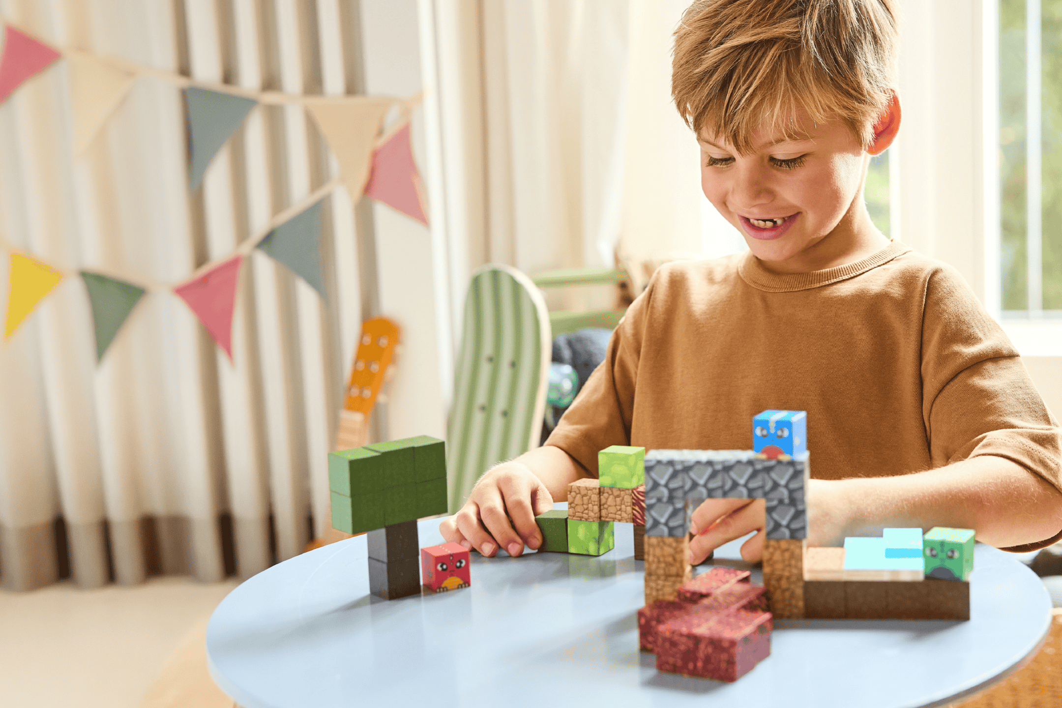 Glad dreng leger med byggeklodser på et bord i et lyst rum med guirlander.
