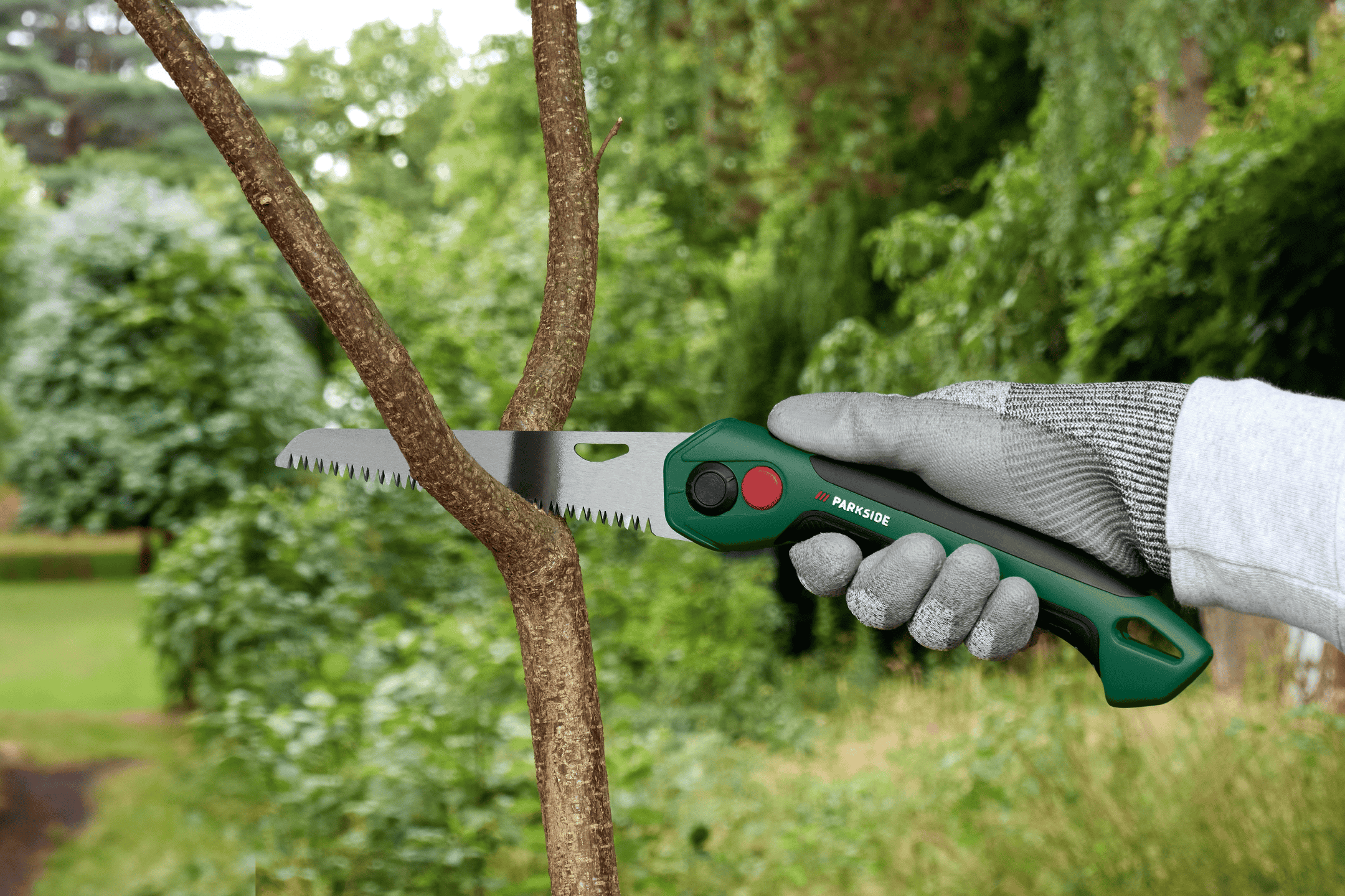 En person i handsker saver en gren af et træ med en grøn sav.