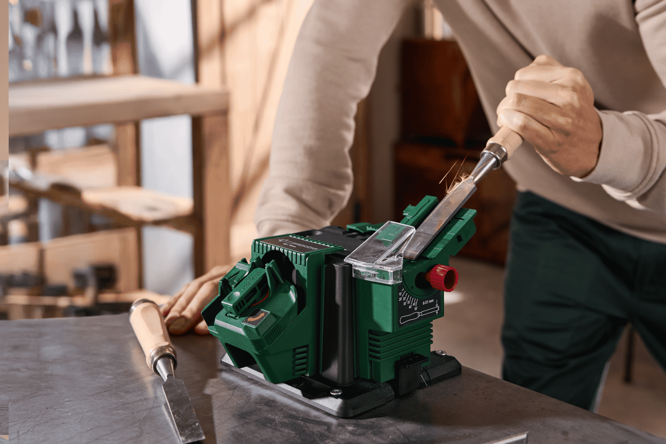 Mand sliber en mejsel med en elektrisk slibemaskine på et værkstedsbord.
