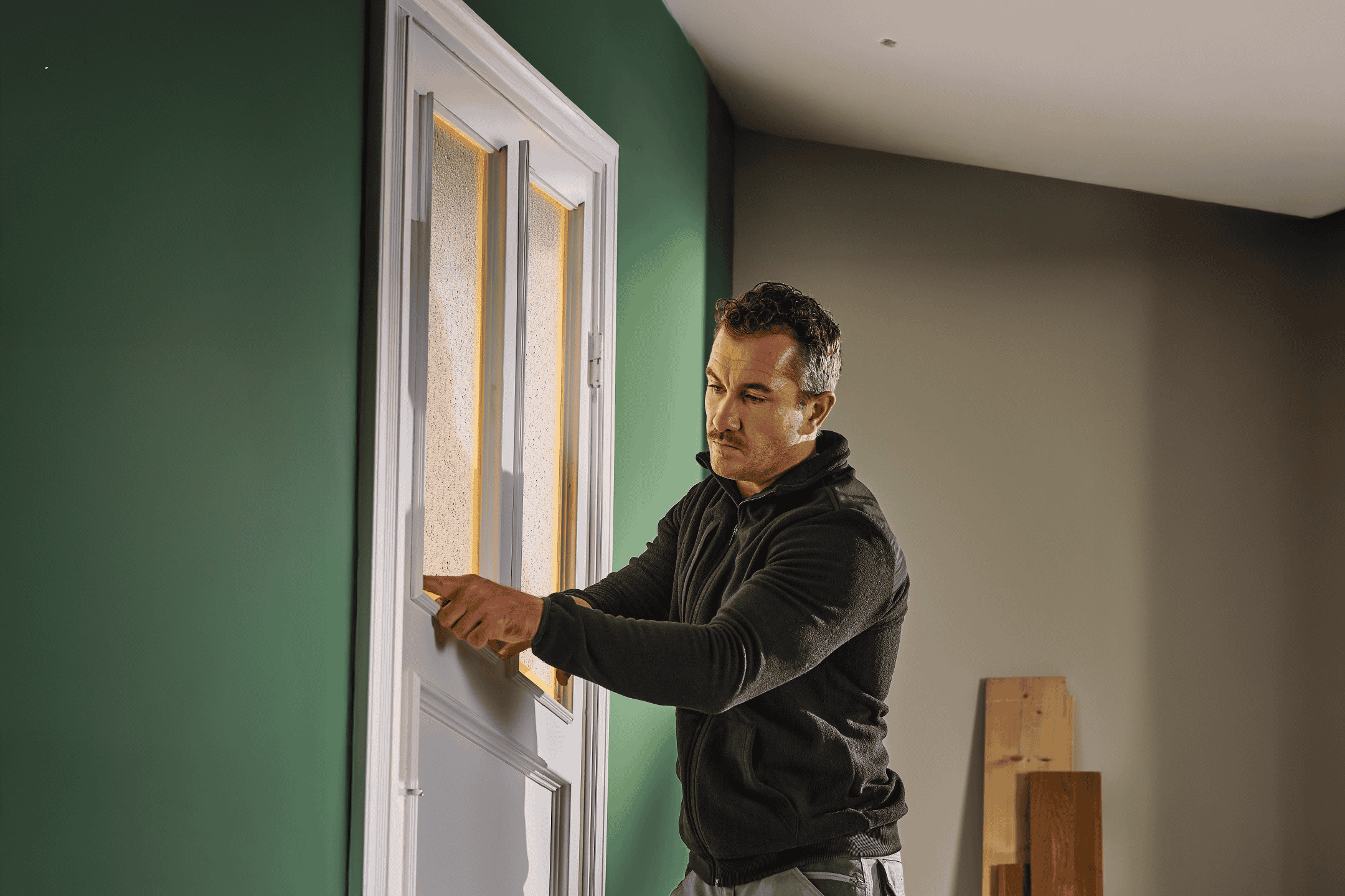 En mand monterer en dør med matteret glas i en grøn væg.