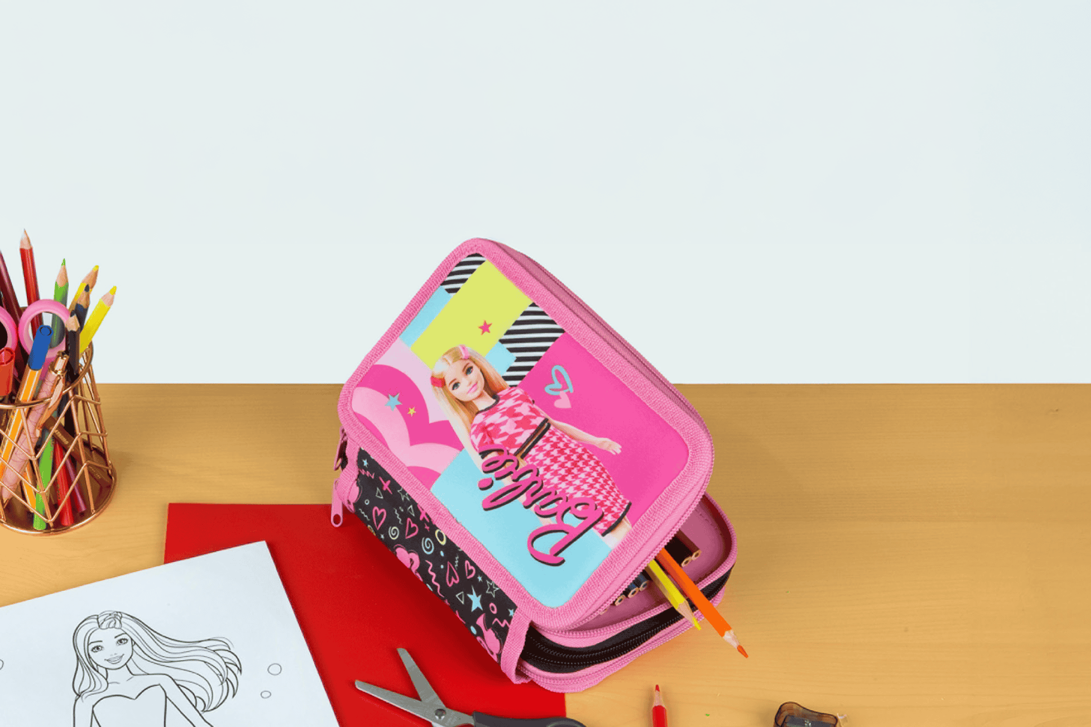 Penalhus med dukke-motiv, farveblyanter og tegneblok på et træbord.