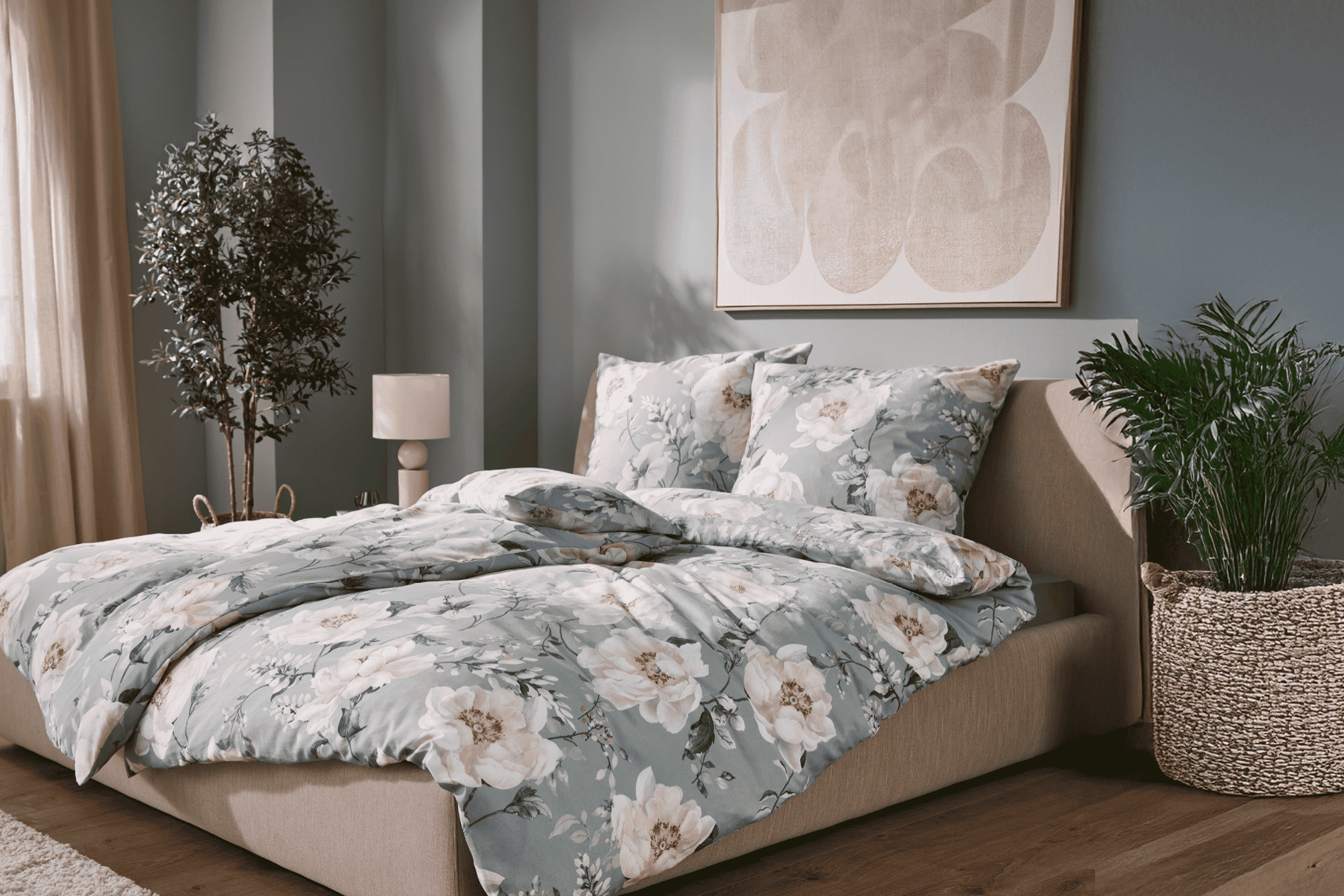 Soveværelse med seng med blomstret sengetøj, to planter og et abstrakt maleri.