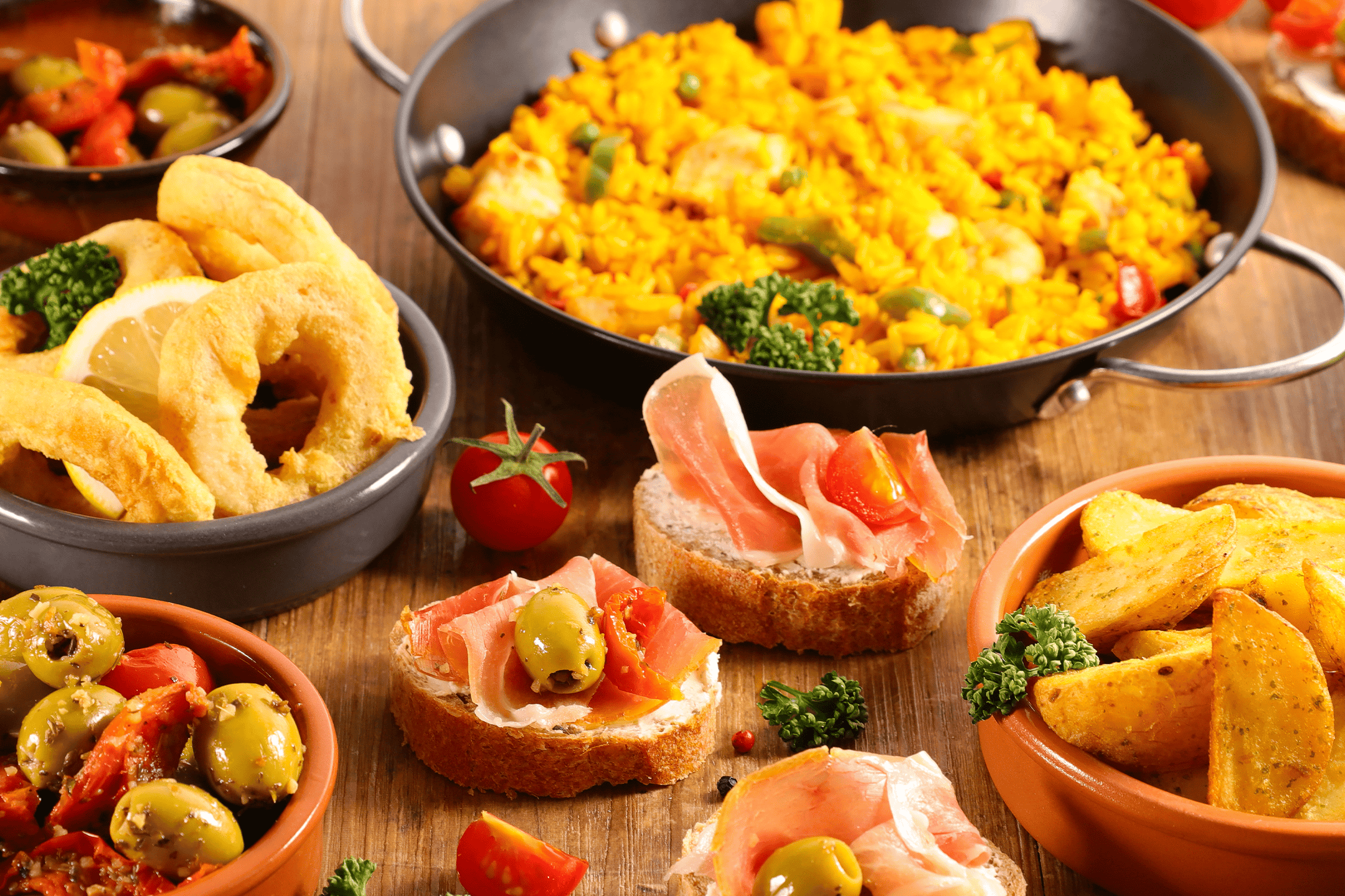 Spansk tapasudvalg med paella, calamari, oliven, patatas bravas og serranoskinke på brød.