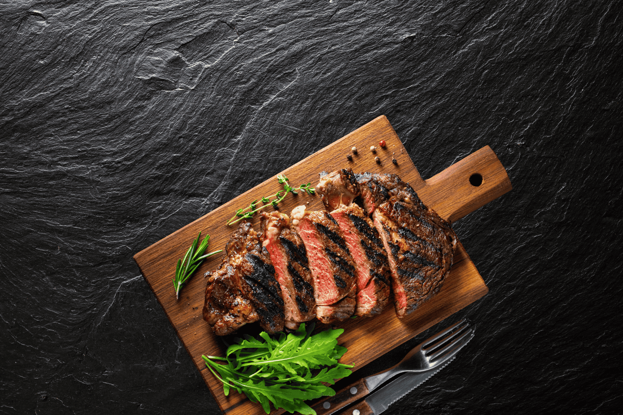 Skåret grillet bøf på et træskærebræt med krydderurter og rucola.