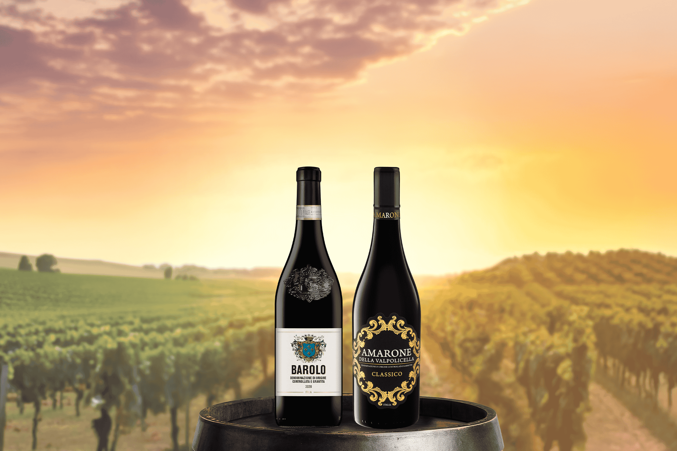 To flasker rødvin, en Barolo og en Amarone Classico, på en vintønde med en vingård i baggrunden.