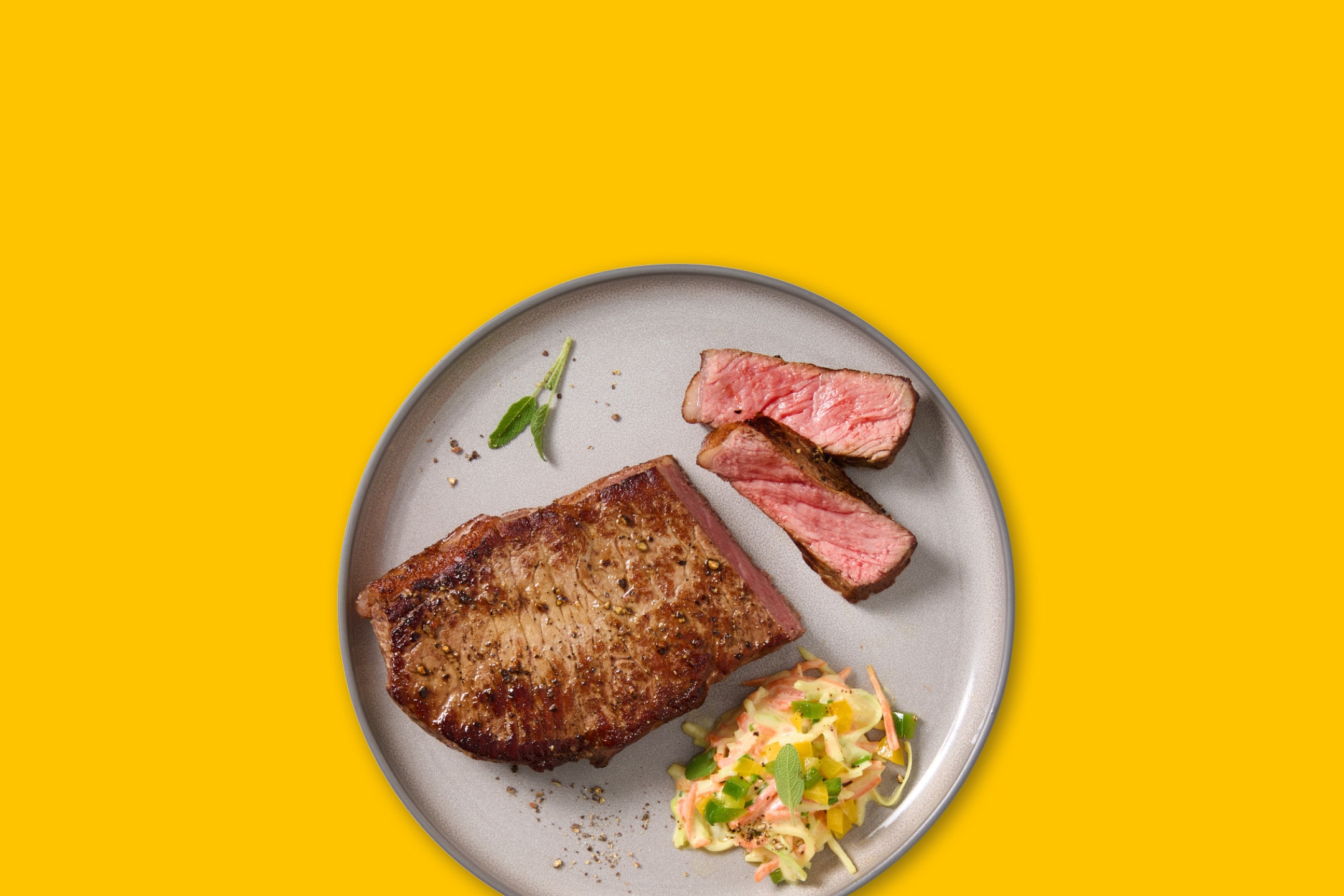 Steak med salat og krydderier på en grå tallerken.
