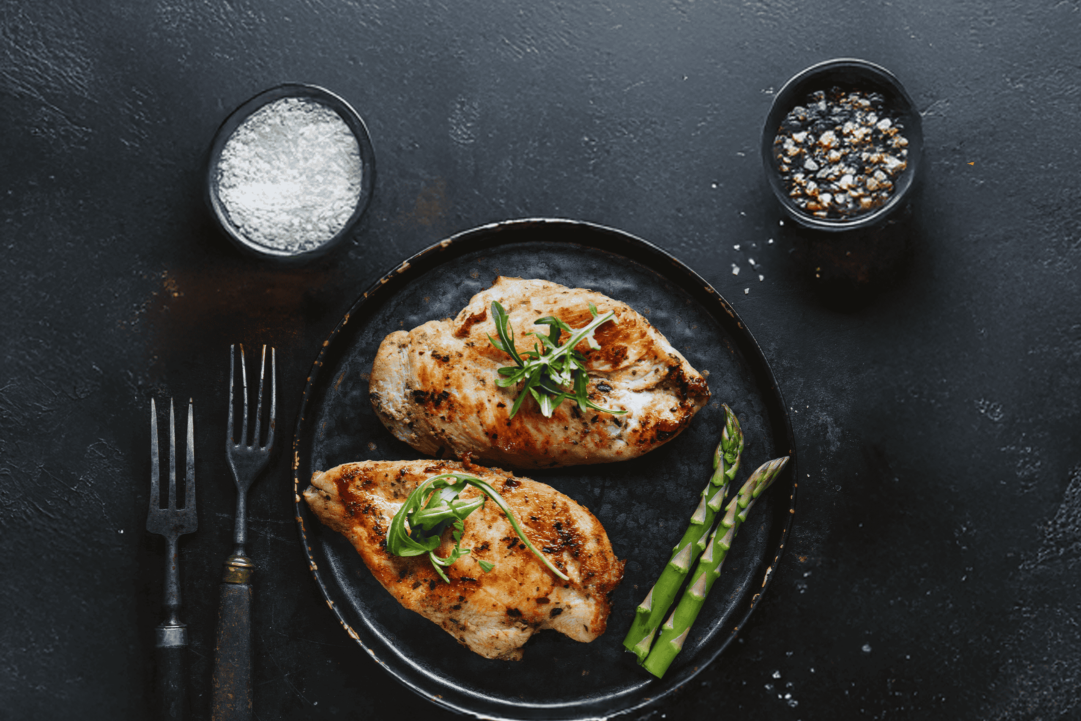 Grillet kyllingebryst med asparges, salt og peber på en mørk baggrund.