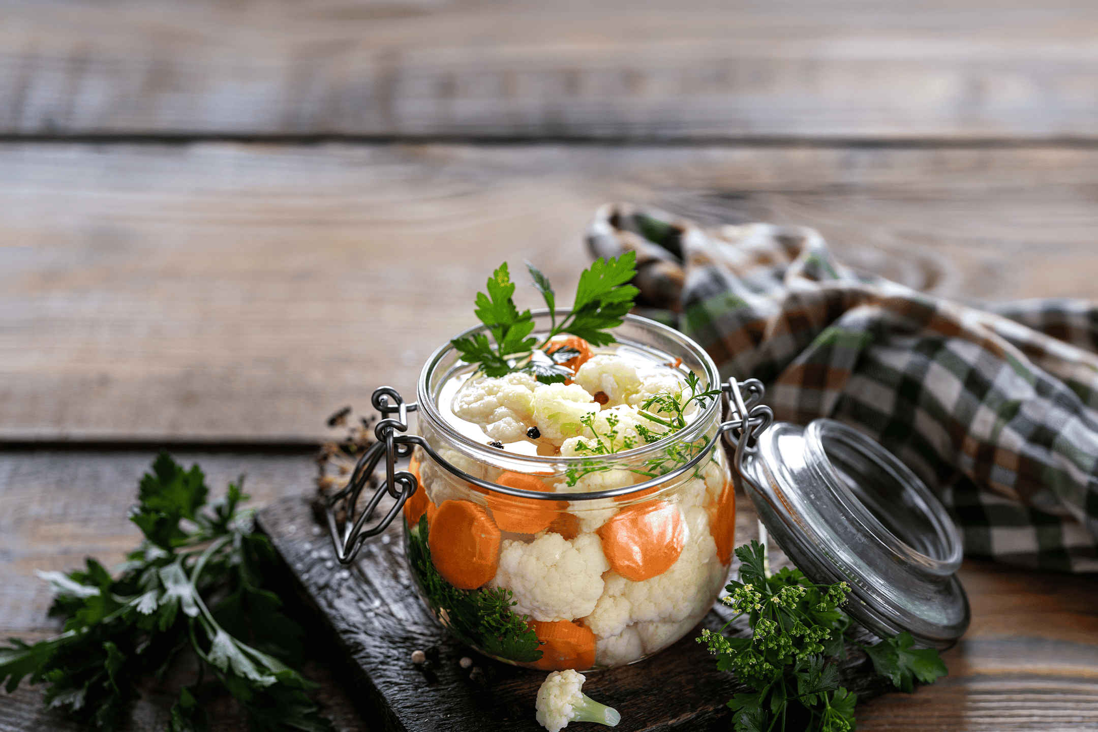 Syltet blomkål og gulerødder i et glas på et træbord.
