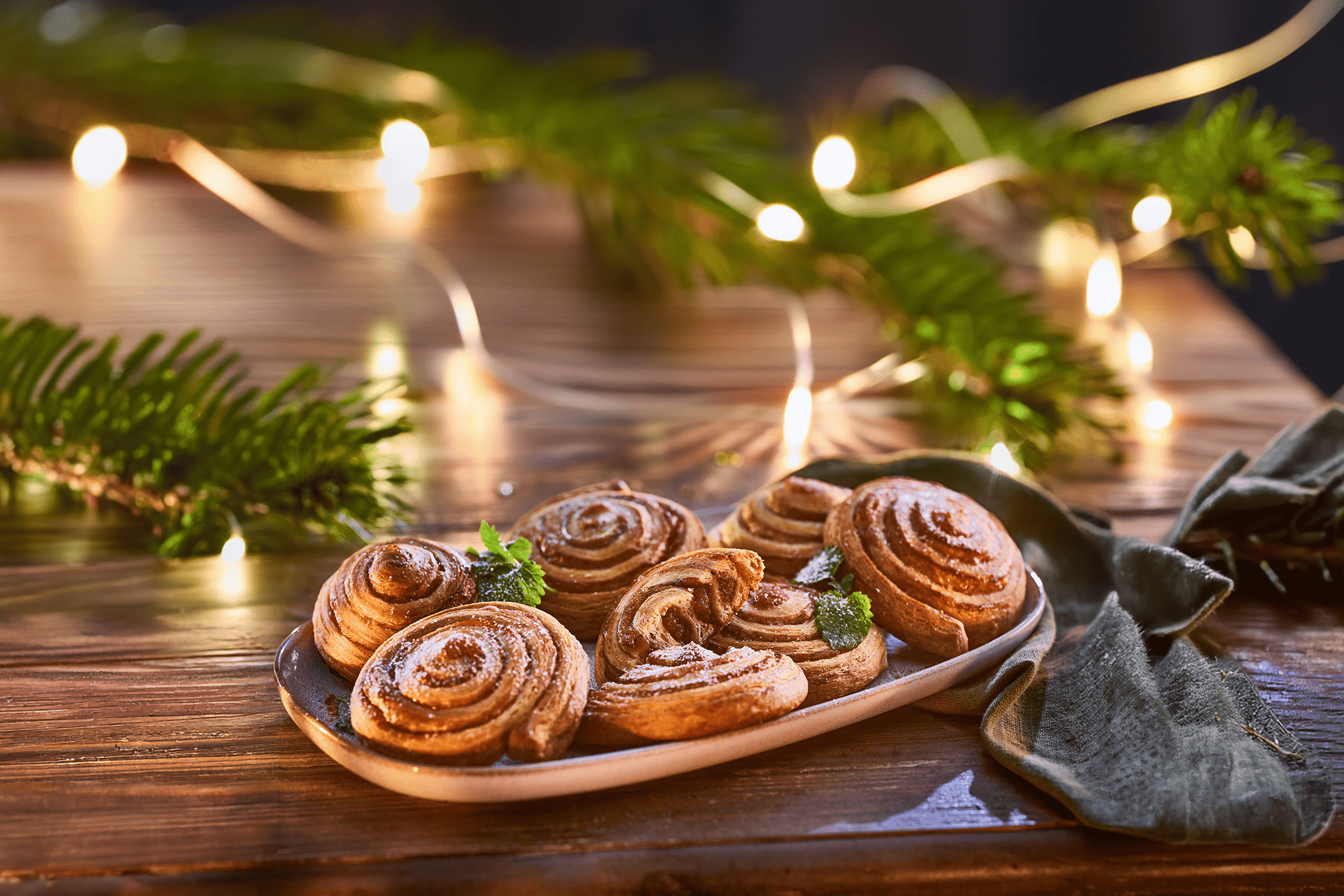 Kanelsnegle på et fad med grangrene og julelys i baggrunden.