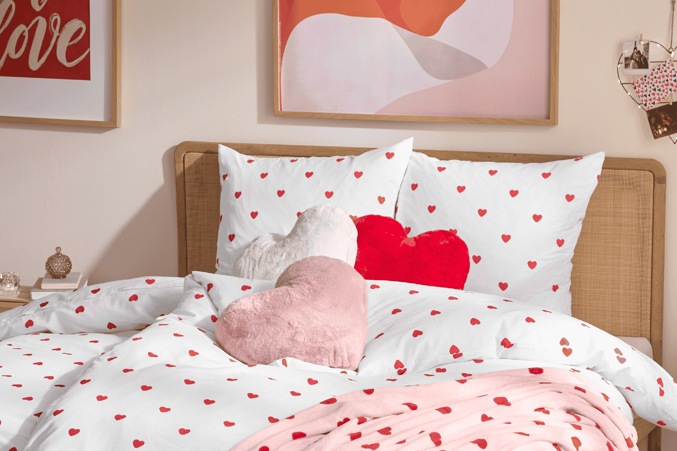 Seng med hvidt sengetøj med røde hjerter, plys hjertepuder og en lyserød plaid.