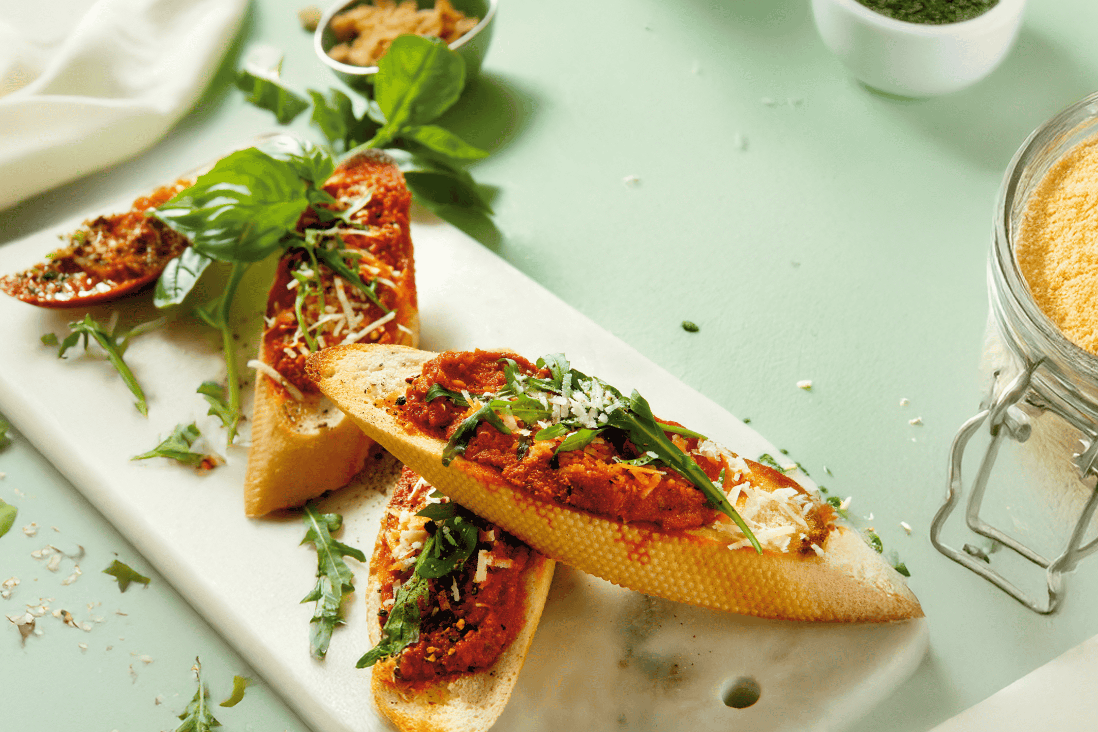 Bruschetta med tomatsauce, rucola og parmesan på et hvidt marmorbræt.