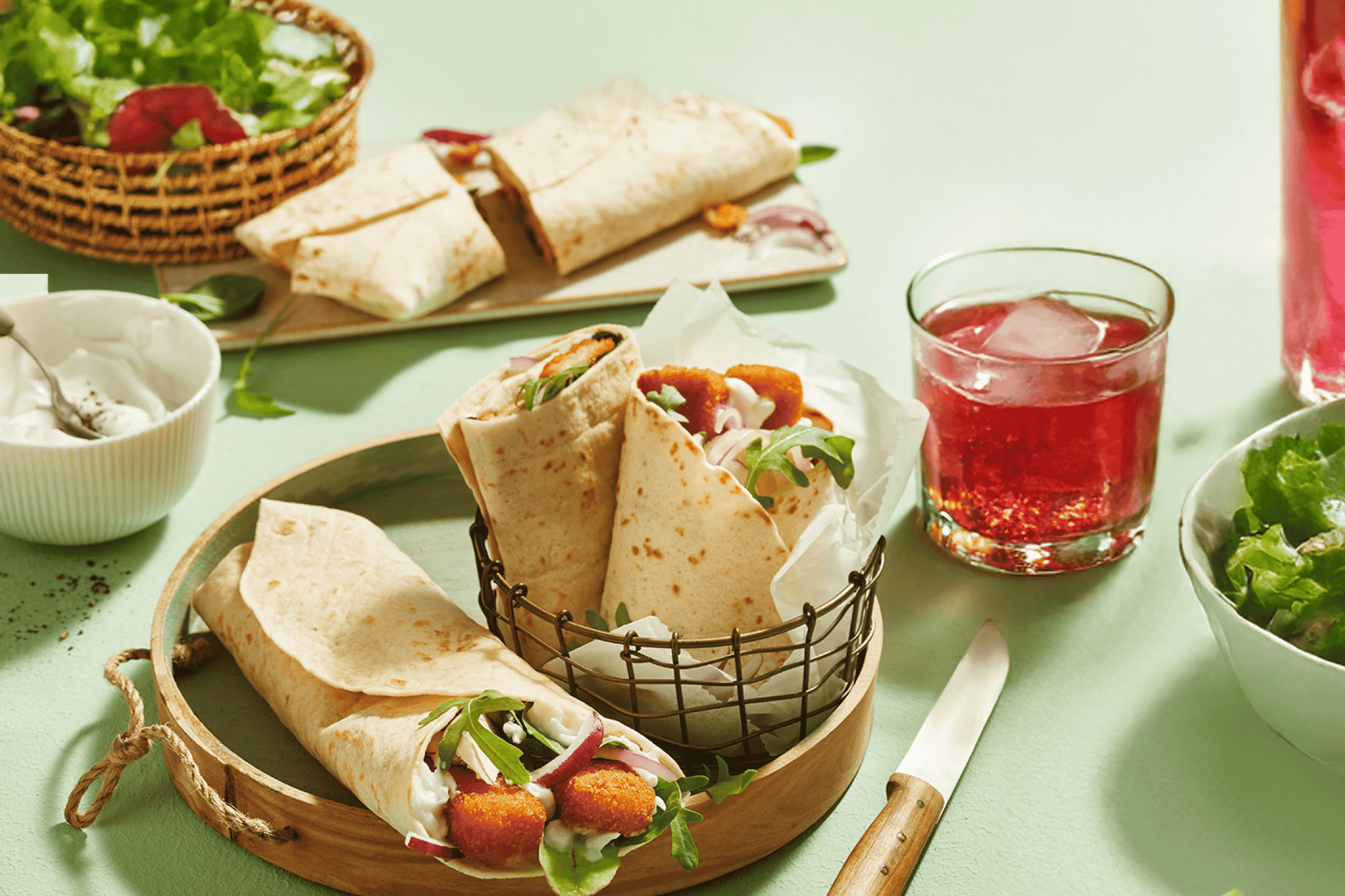 Tortilla-wraps med sprøde nuggets, salat og rødløg, serveret med en rød drink.