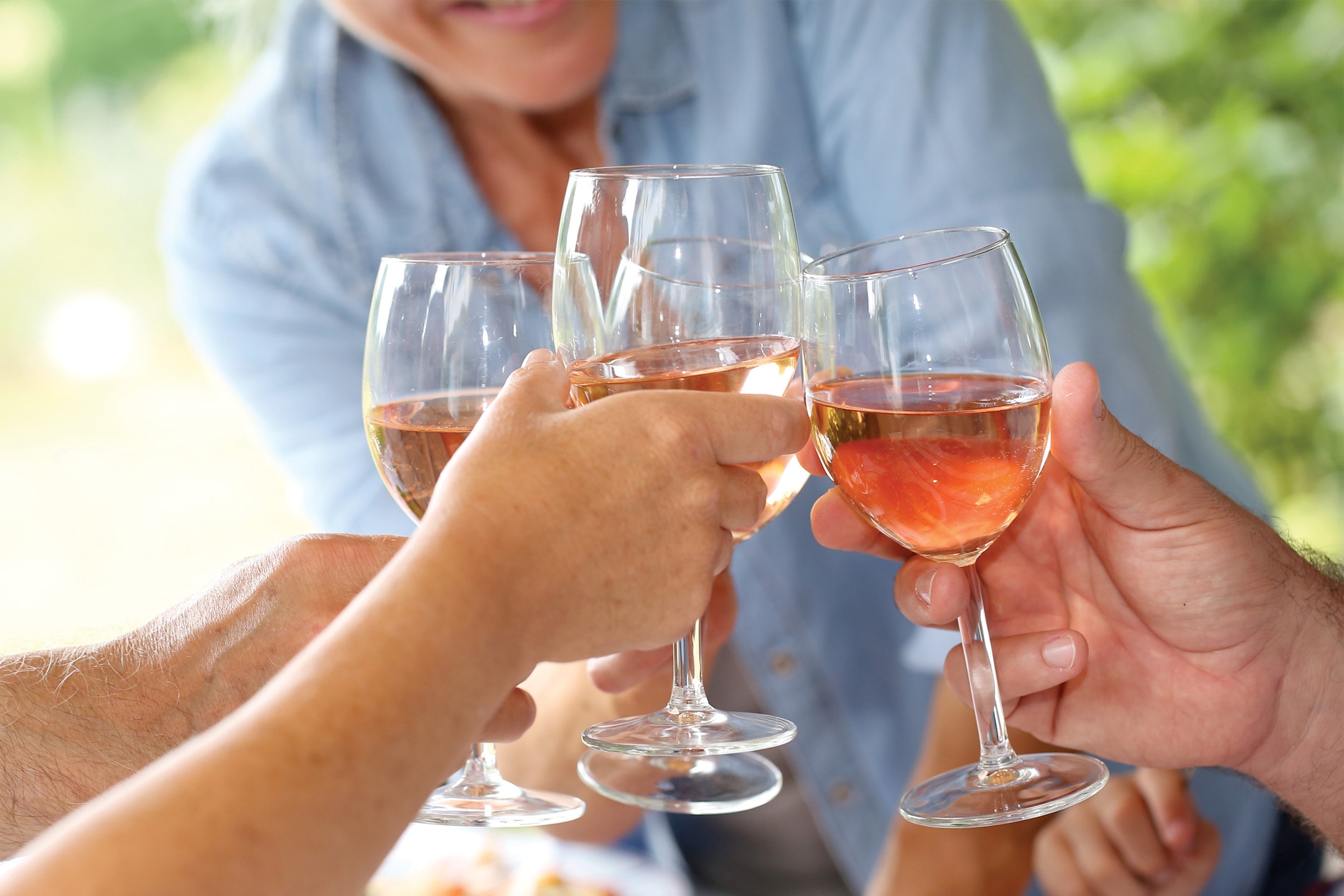 Fire personer skåler med glas fyldt med rosévin udendørs.