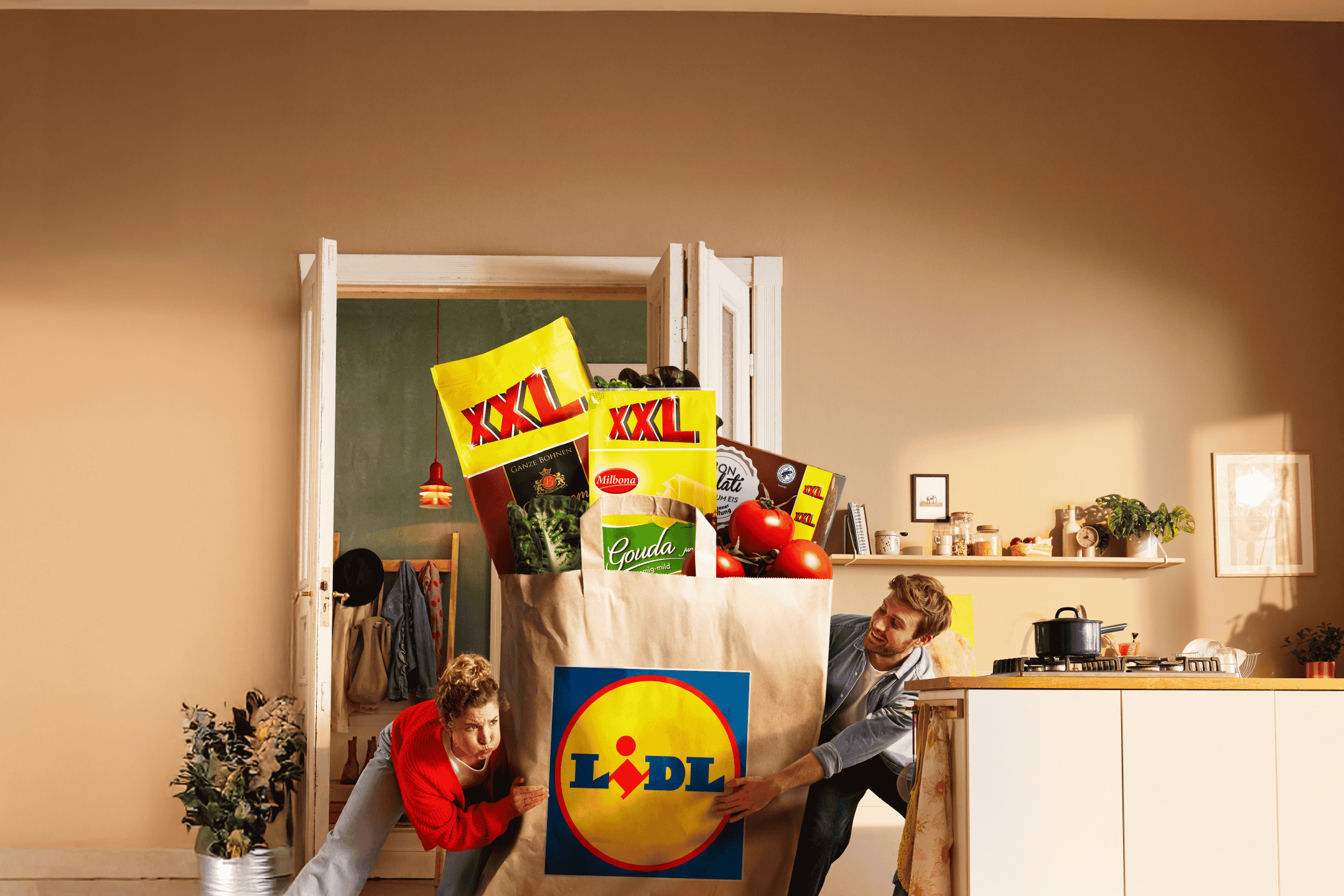 To personer bærer en stor Lidl-pose fyldt med XXL-produkter, Gouda-ost og tomater.