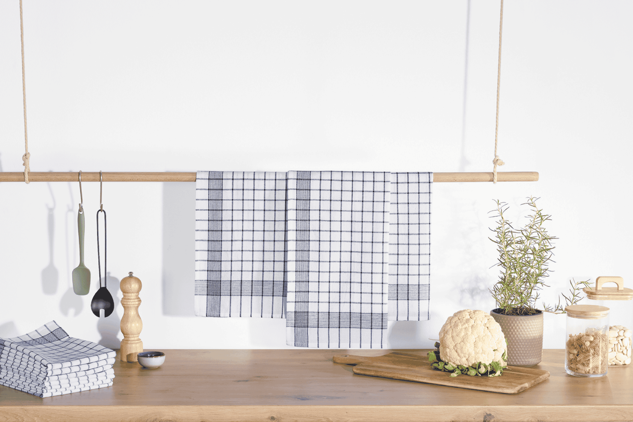 Køkkenhåndklæder, køkkenredskaber, krydderkværn, blomkål og opbevaringsglas på træbord.