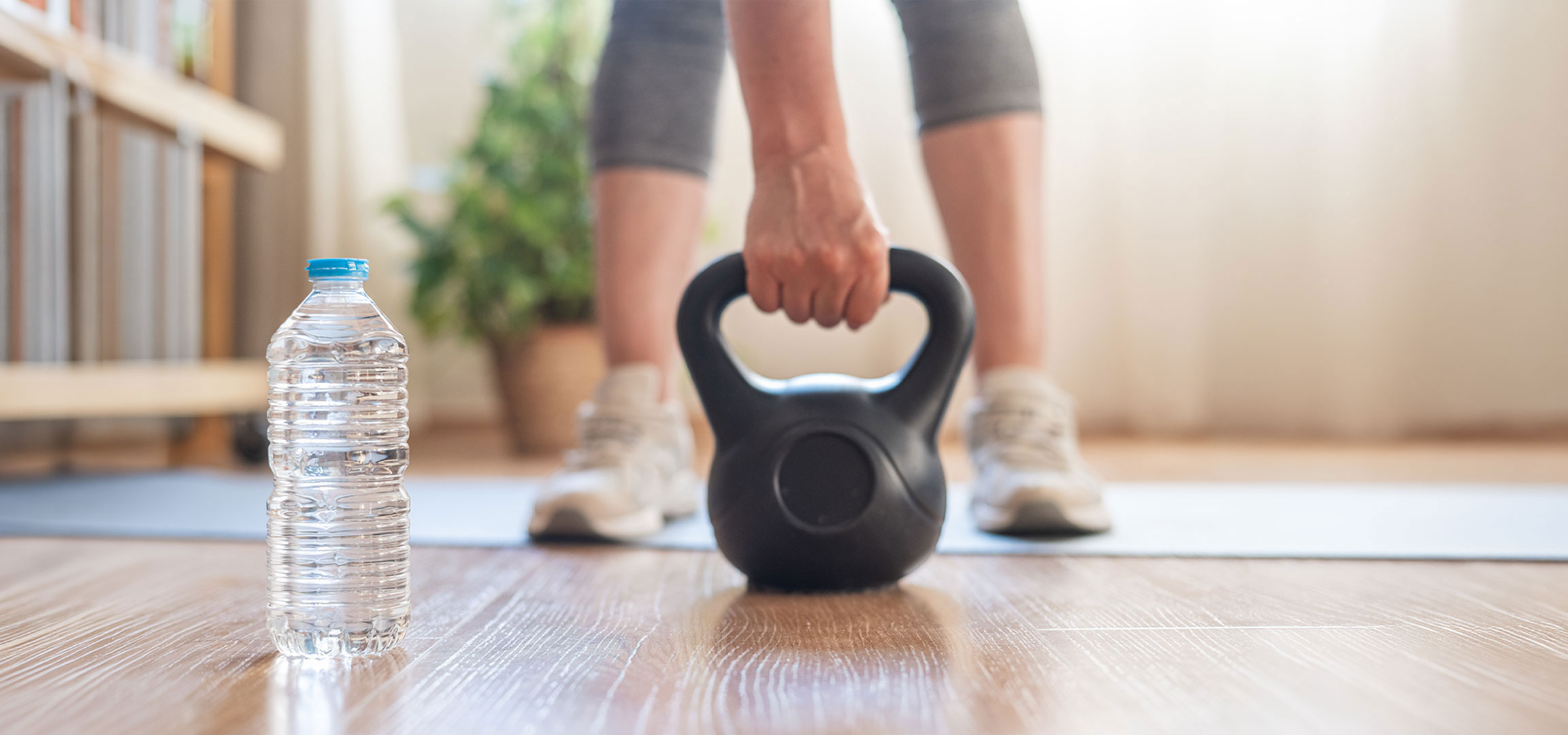 aiLabeling.aiLabelForImageAltText: Kvinde gør sig klar til at træne med en kettlebell og en vandflaske på en yogamåtte.
