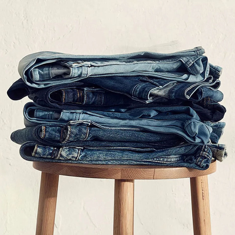 En bunke jeans i forskellige blå nuancer på en træskammel.