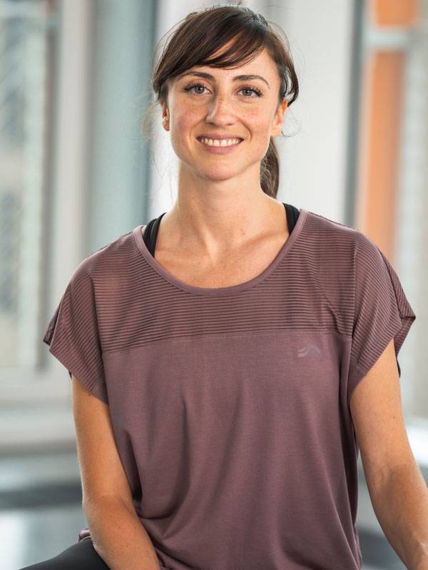 Smilende kvinde iført en kortærmet lilla sportstop.