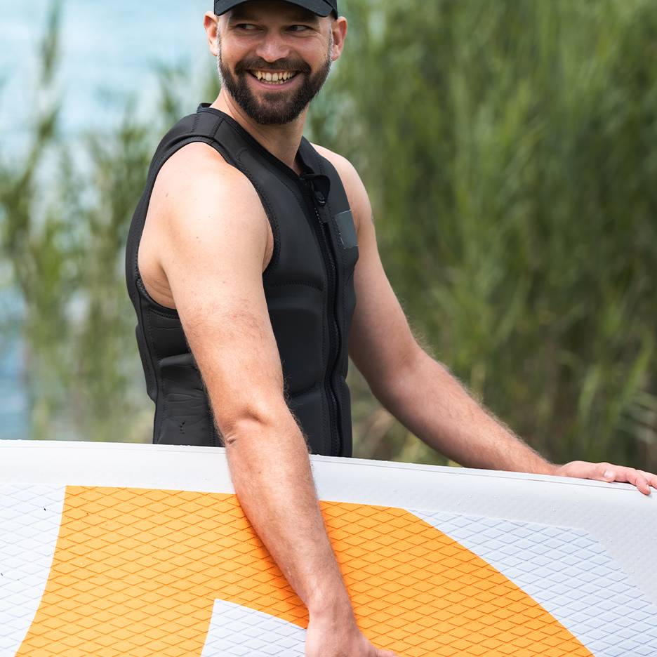 Smilende mand i sort redningsvest holder et paddleboard.