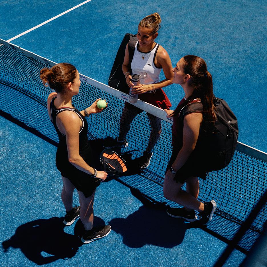 Agostina Bigotti og to medspillere i CRIVIT-sportstøj står sammen ved padelnettet på en blå bane efter kampen.