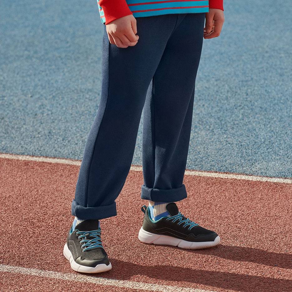 Mørkeblå joggingbukser og sorte sneakers med blå snørebånd på en løbebane.