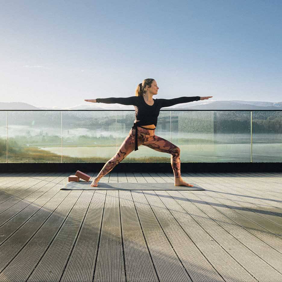 Kvinde i træningstights og top dyrker yoga på en terrasse med udsigt.