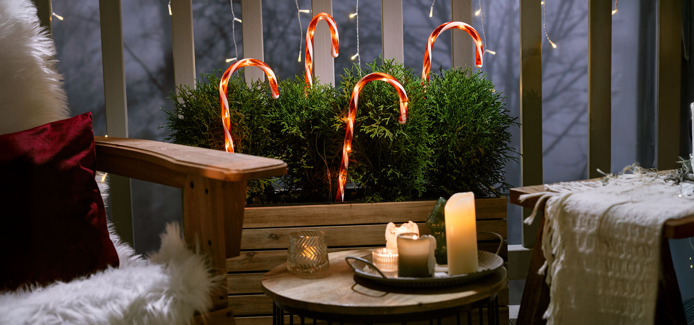 Julepyntet balkon med en stol, stearinlys og slikstokke.