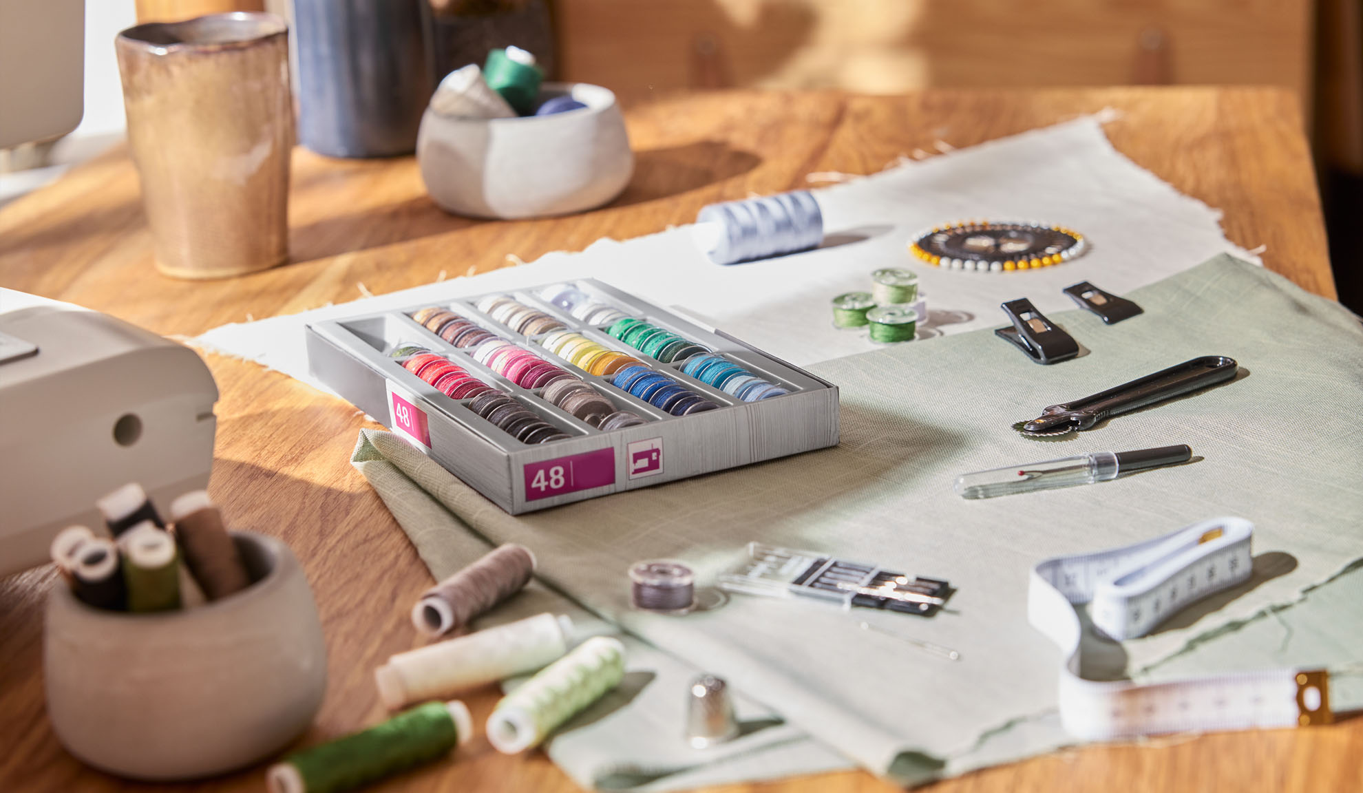 Sysæt med en æske farverige tråde, symaskine og diverse værktøjer på et træbord.