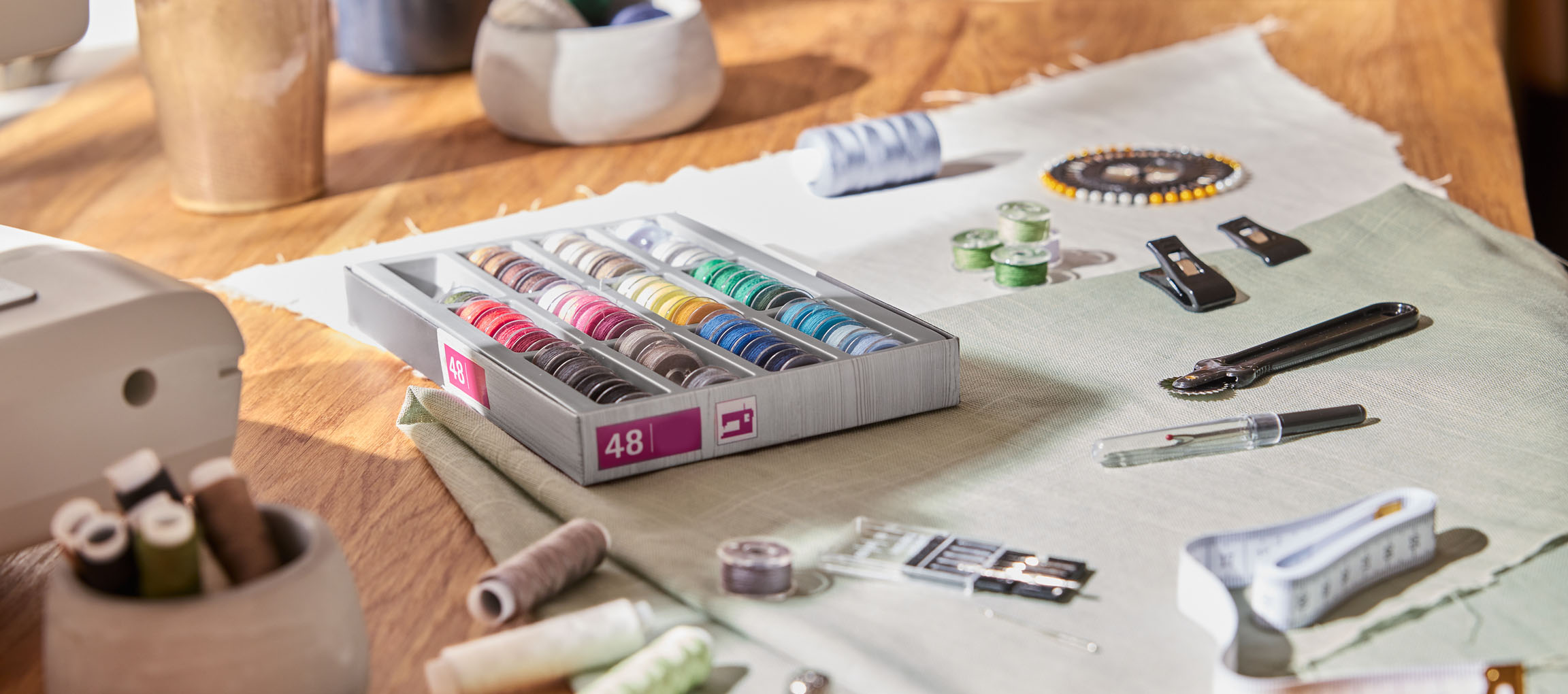 Syartikler på et træbord, inklusive en trådorganisator med 48 spoler, stof og diverse værktøjer.