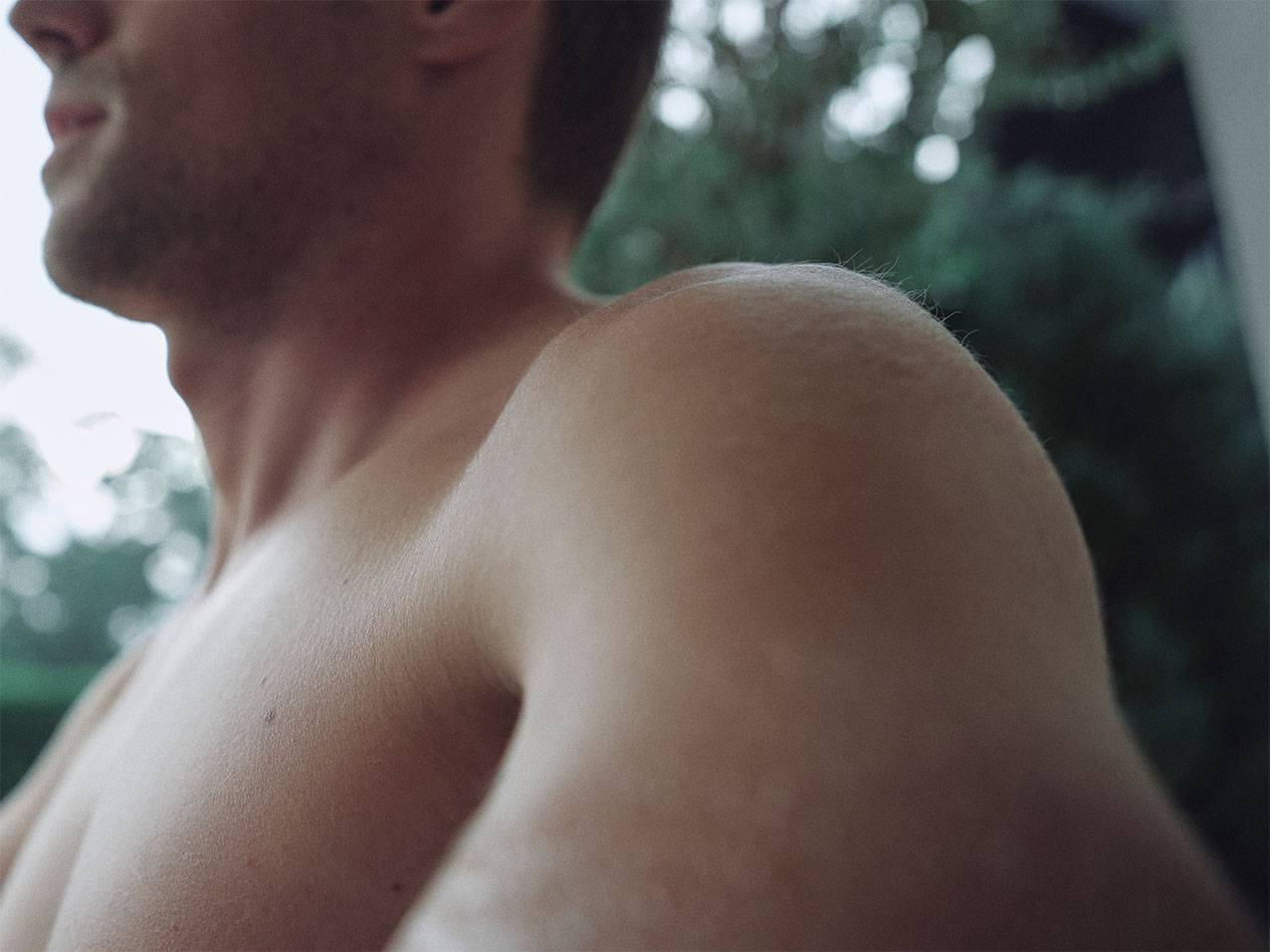 Nærbillede af en mands skulder og hals, med en sløret grøn baggrund.