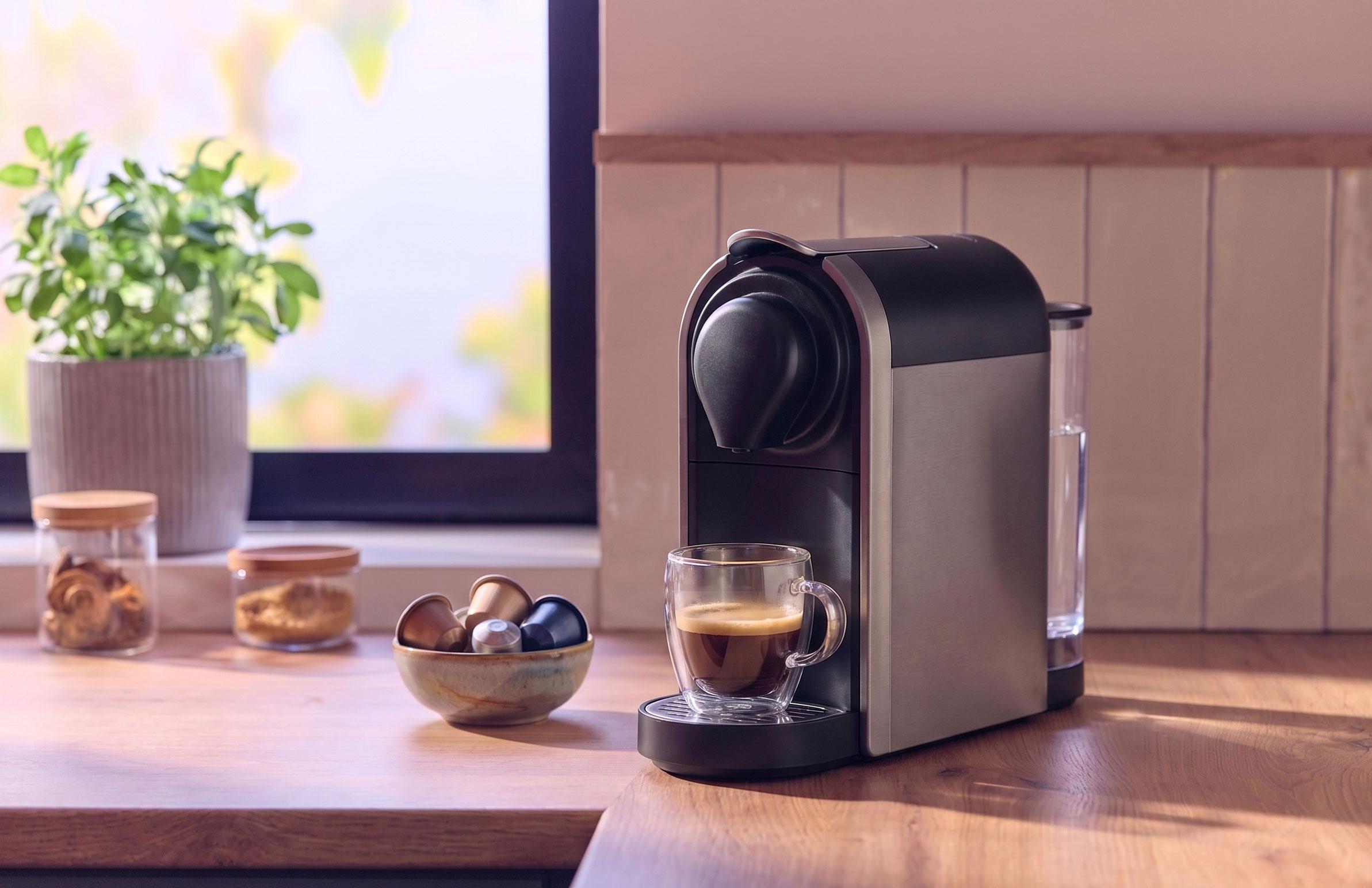Kaffemaskine med en kop kaffe, kapsler og krukker på en træbordplade.