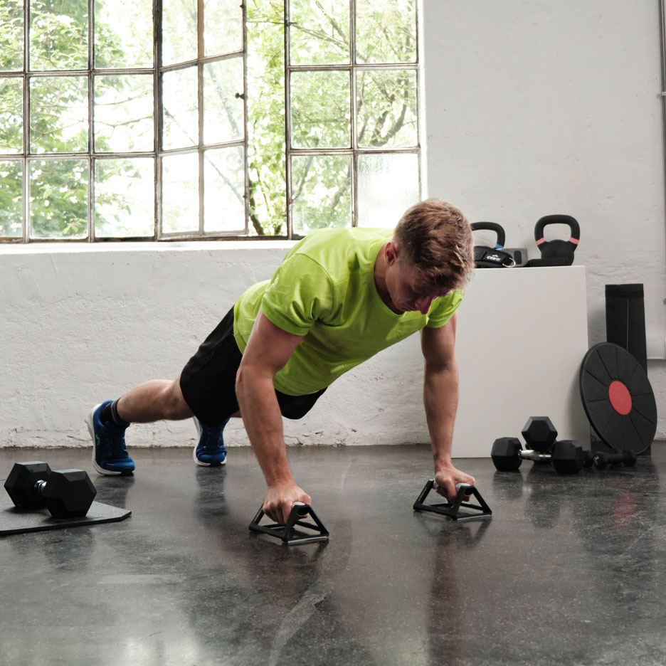 Mand der laver armstrækninger med håndtag i et fitnesscenter.