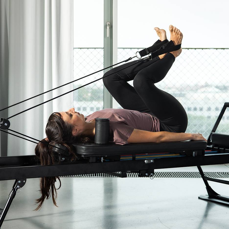 Kvinde træner ben på en Pilates reformer med modstandsbånd.