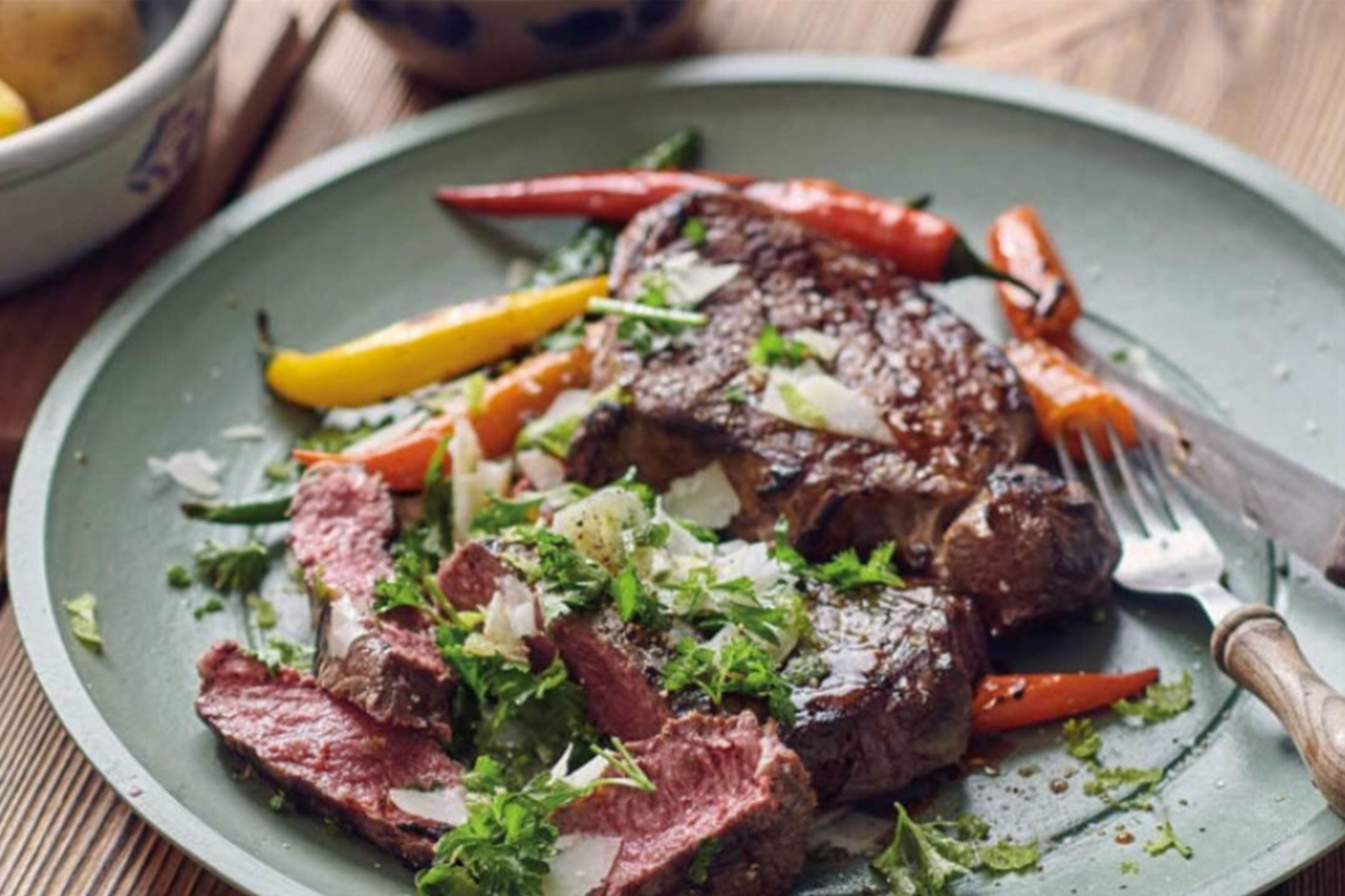 Grillet bøf med peberfrugter, friske krydderurter og revet ost på en grøn tallerken.